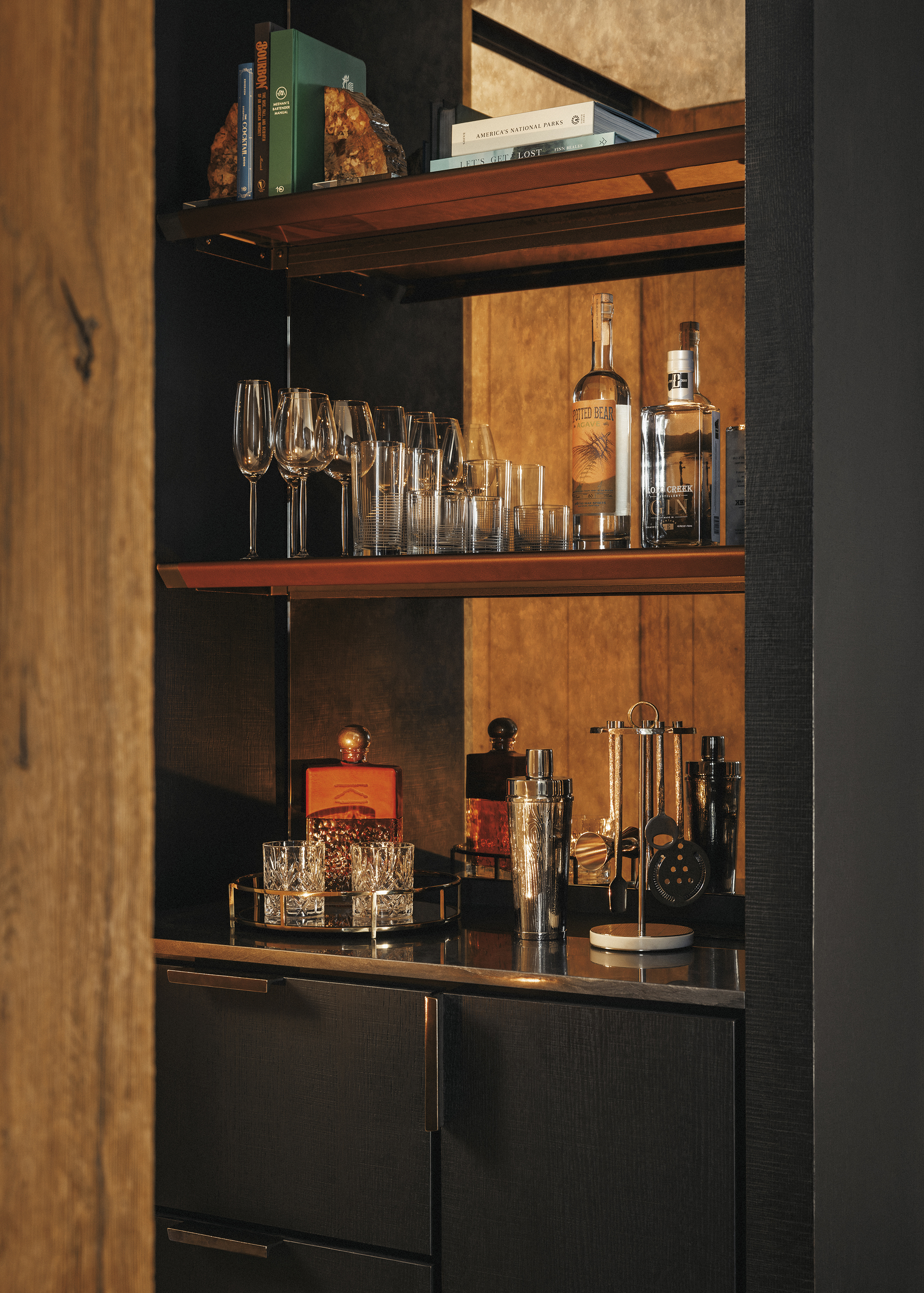 A close up of bar shelves featuring glasses, cocktail mixers, spirit bottles and decorative items
