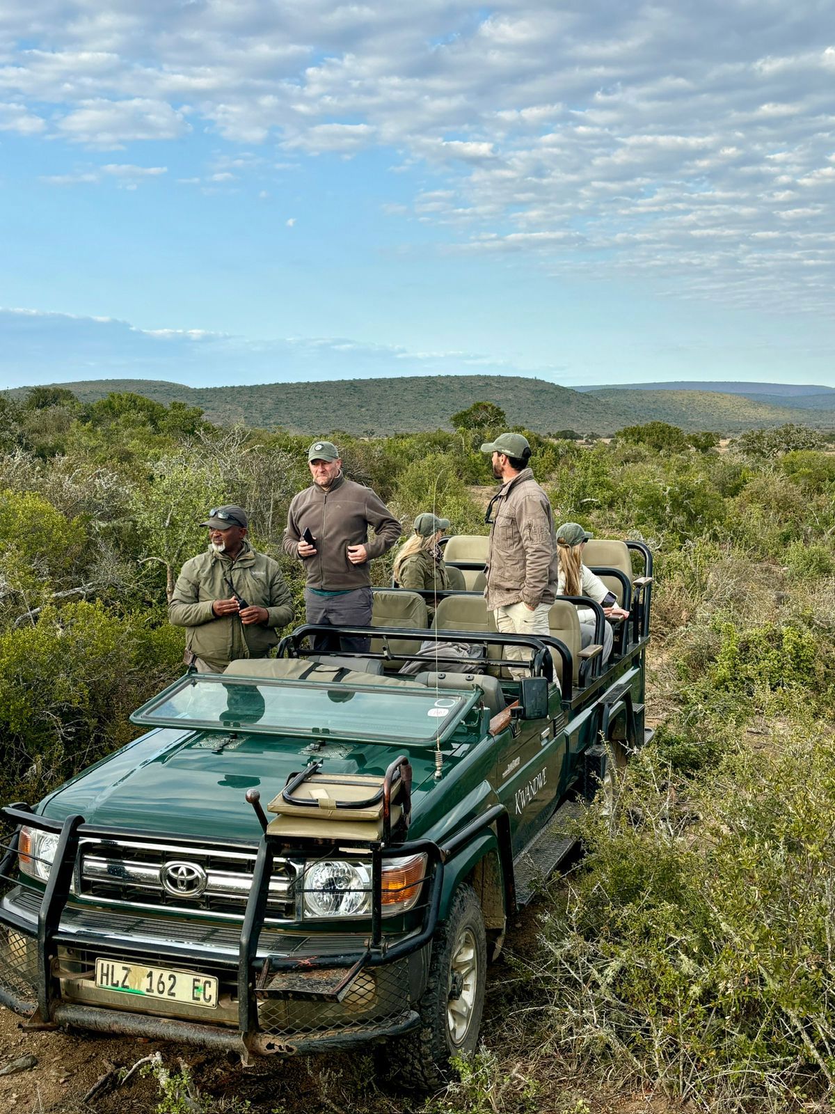 Green jeep with five people on a conservation drive parked in the land of Kwandwe Private Game Reserve