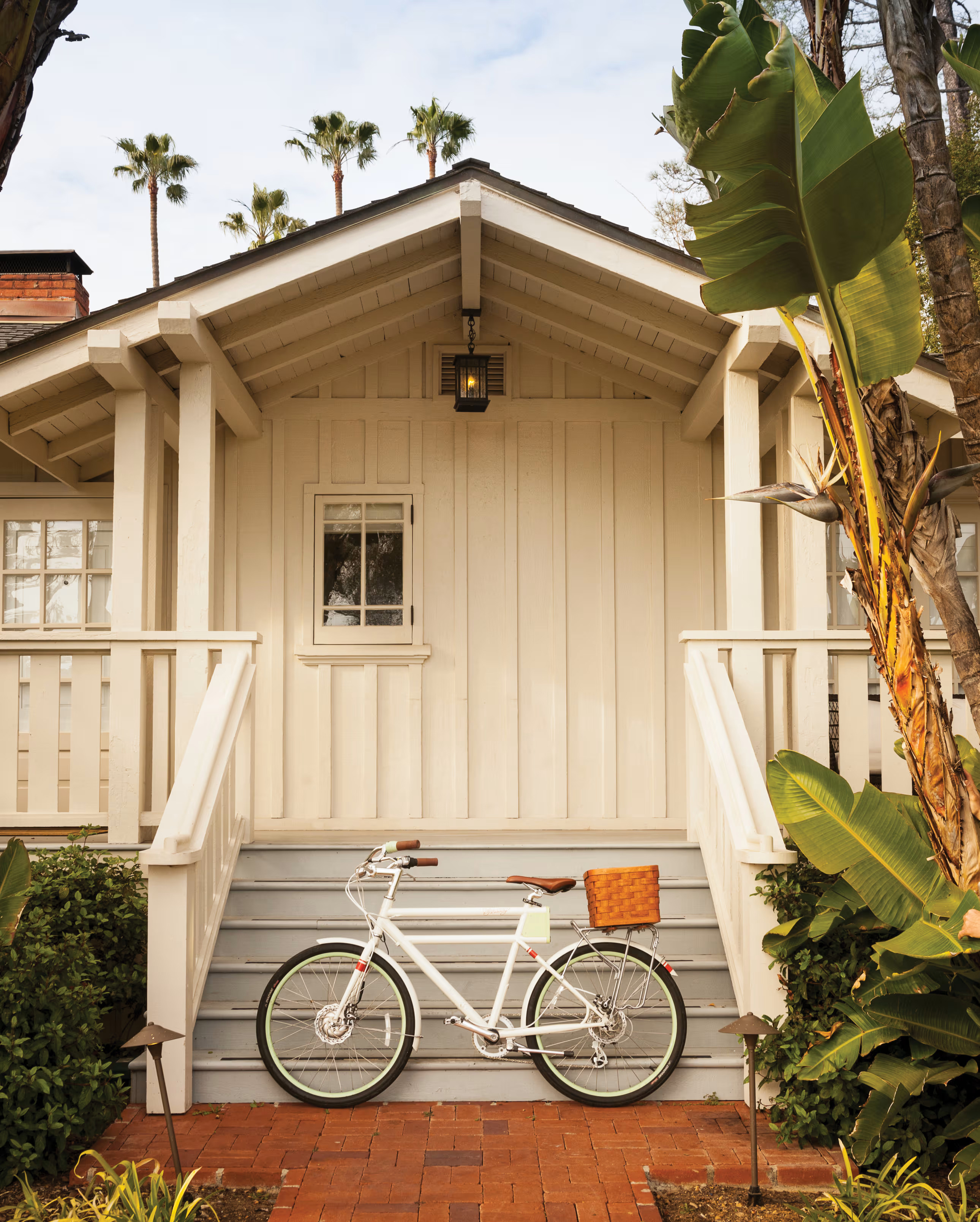 A bike parked at the bottom of steps leading up to a white wooden building flanked by palms