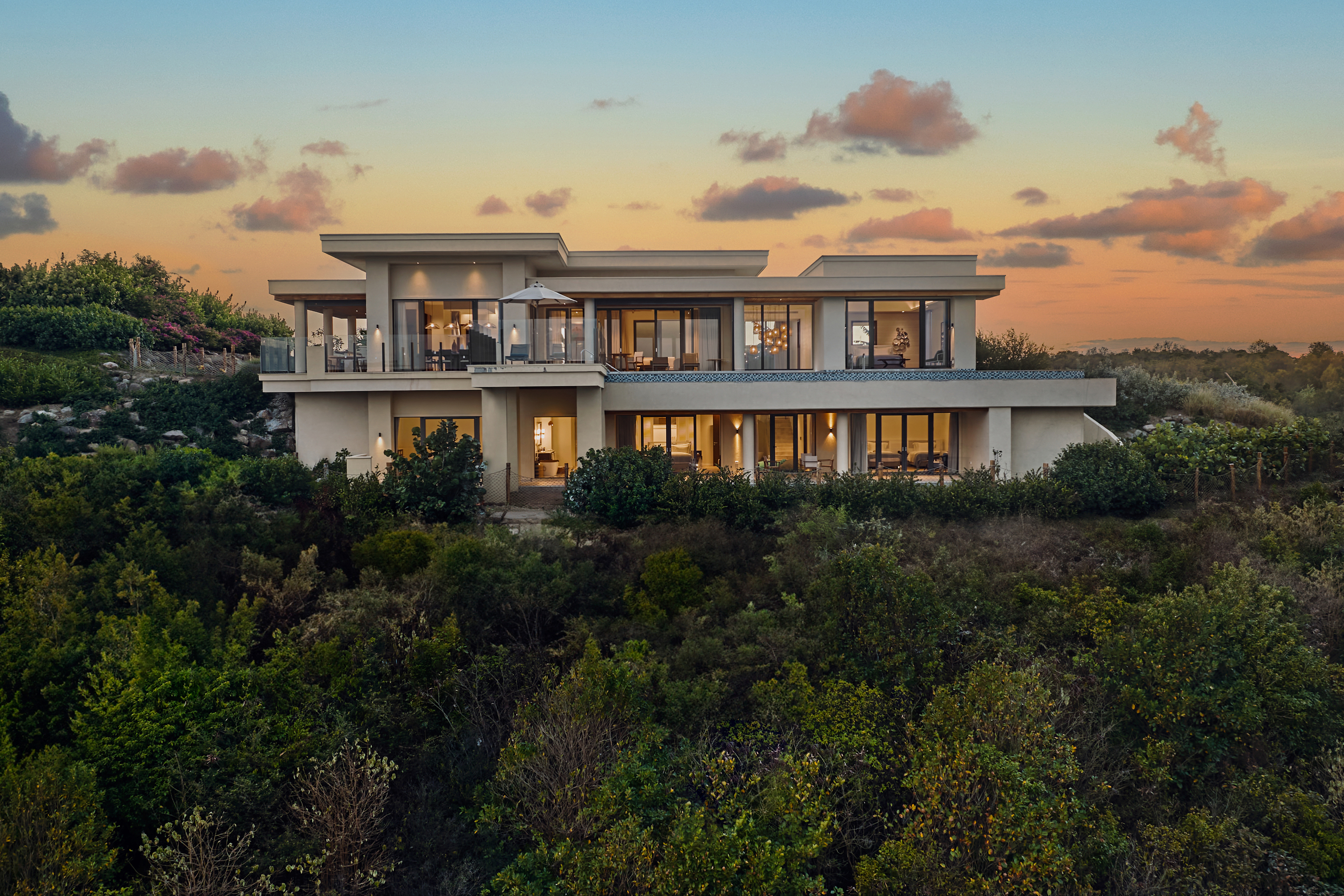 A large villa with 2 storeys is surrounded by greenery and palm trees