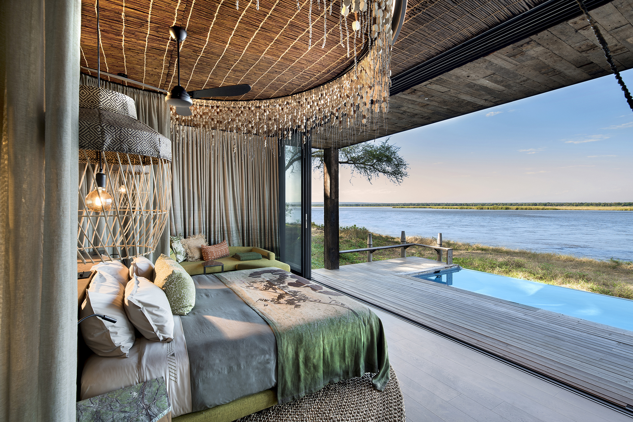 A bedroom at Lolebezi featuring a comfy bed with large overhanding headboard and a deck with a pool and view of the river