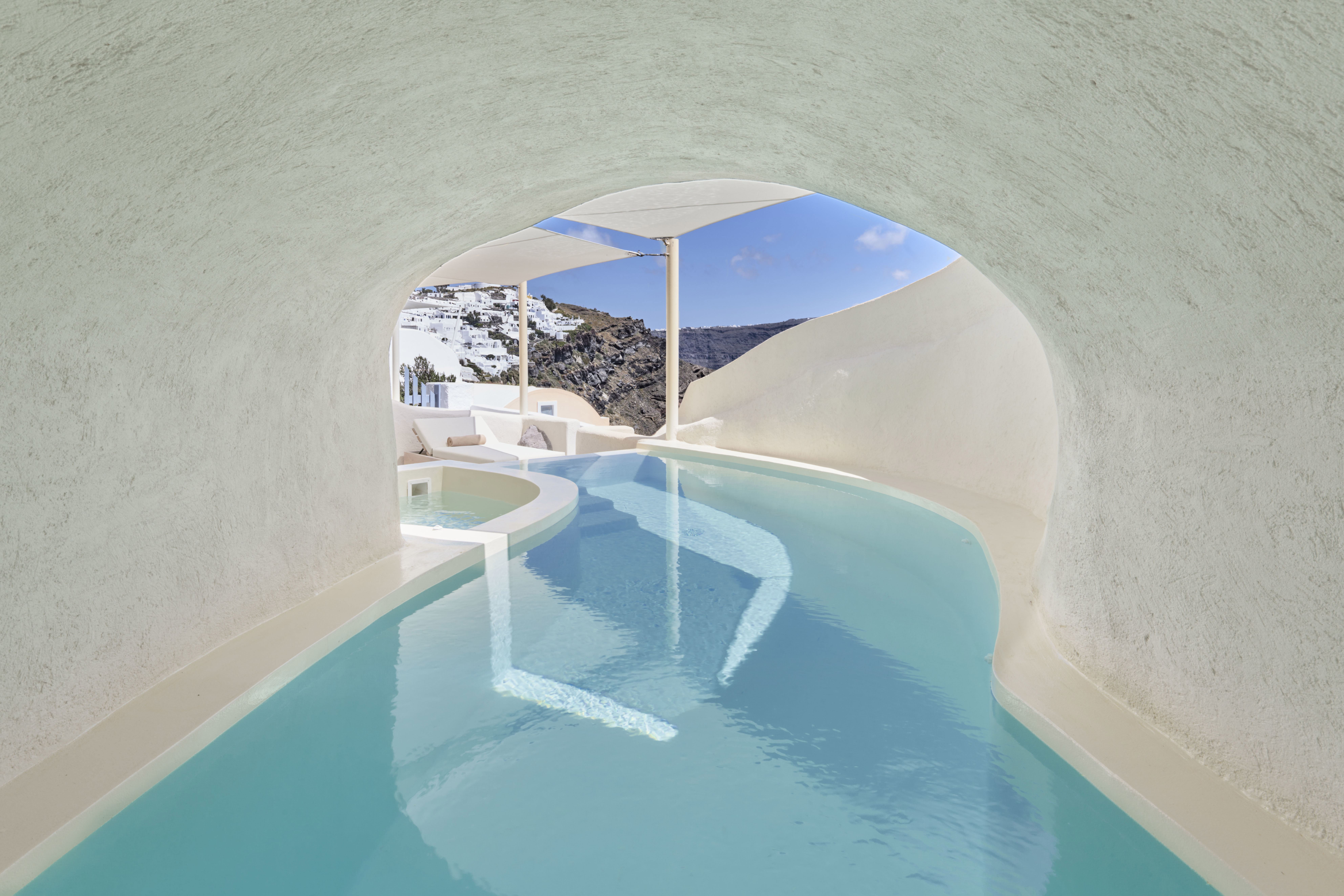 The swimming pool of a Cave Suite running beneath a white arch to a terrace outside