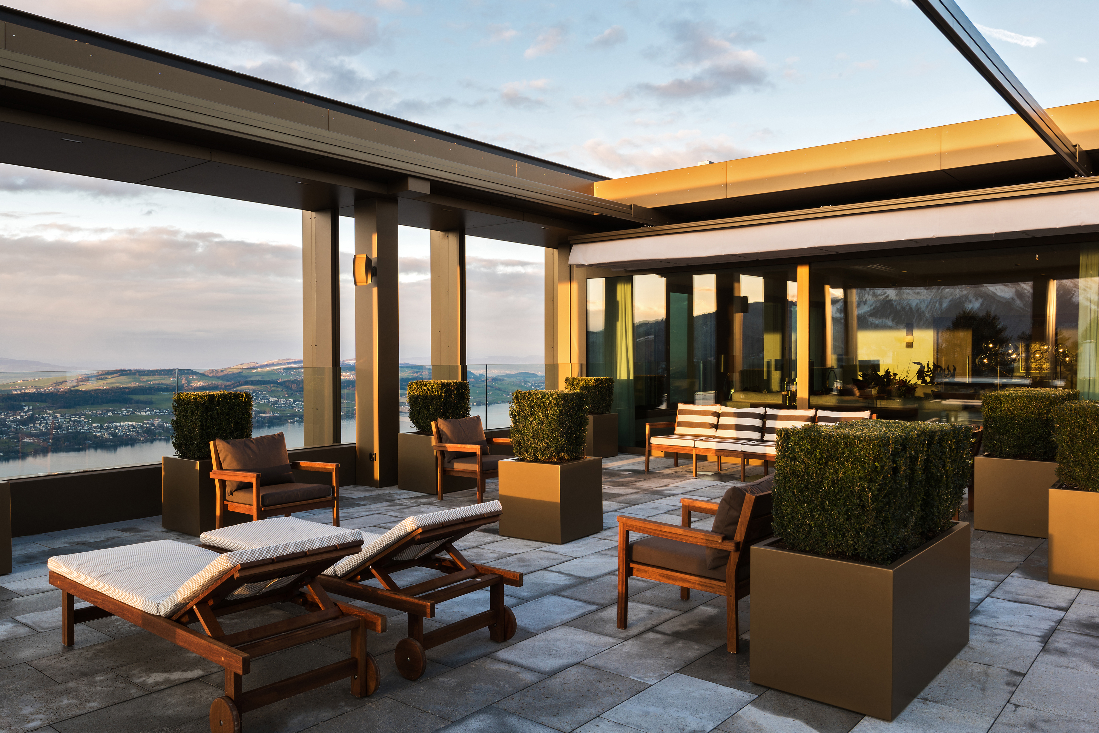 The outdoor terrace of a LAke View Royal Suite at Bürgenstock Hotel with stylish outdoor furniture and sun loungers surrounded by potted shrubbery 