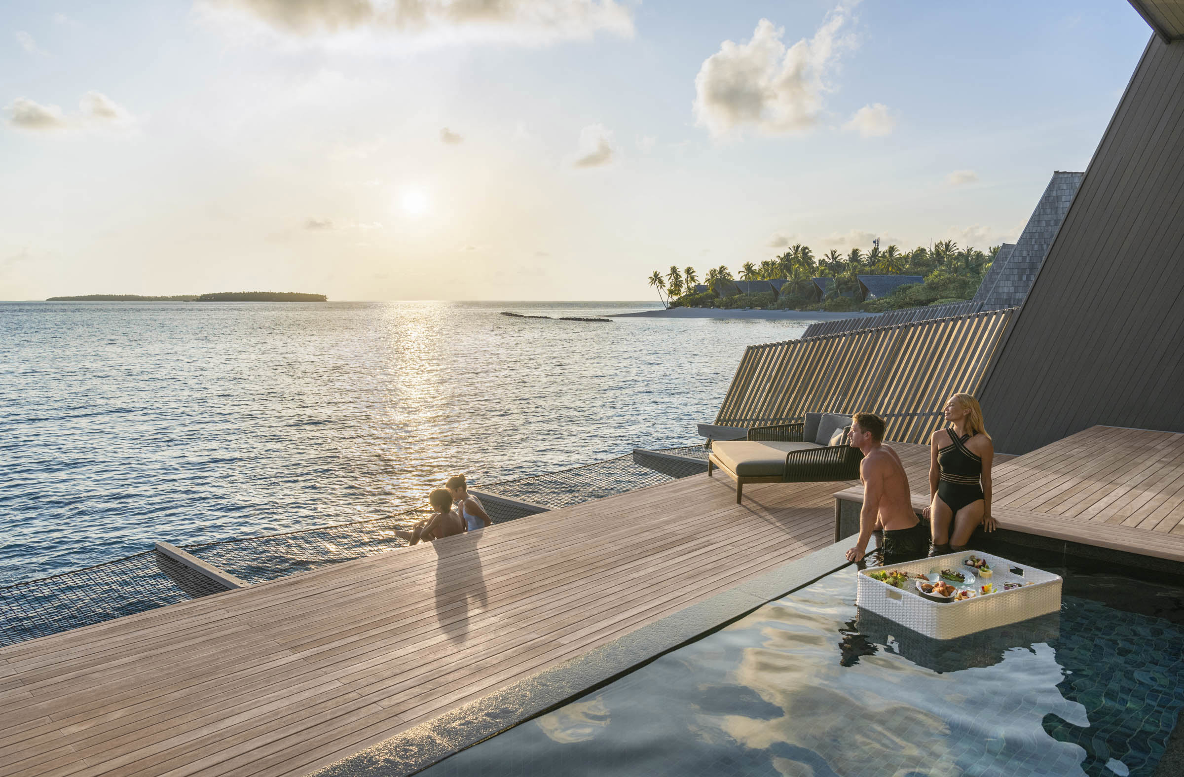 A family of four relaxing in a villa pool at The St. Regis Maldives Vommuli Resort overlooking the sea with a floating breakfast tray