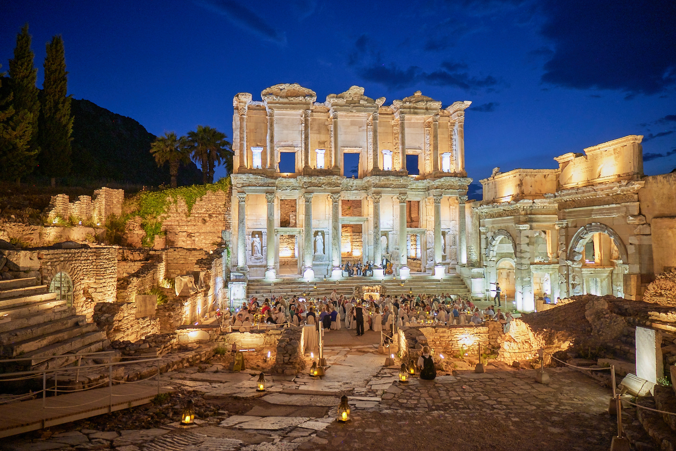 Ruins of an ancient Roman structure lit up at night with a crowd of people gathered below
