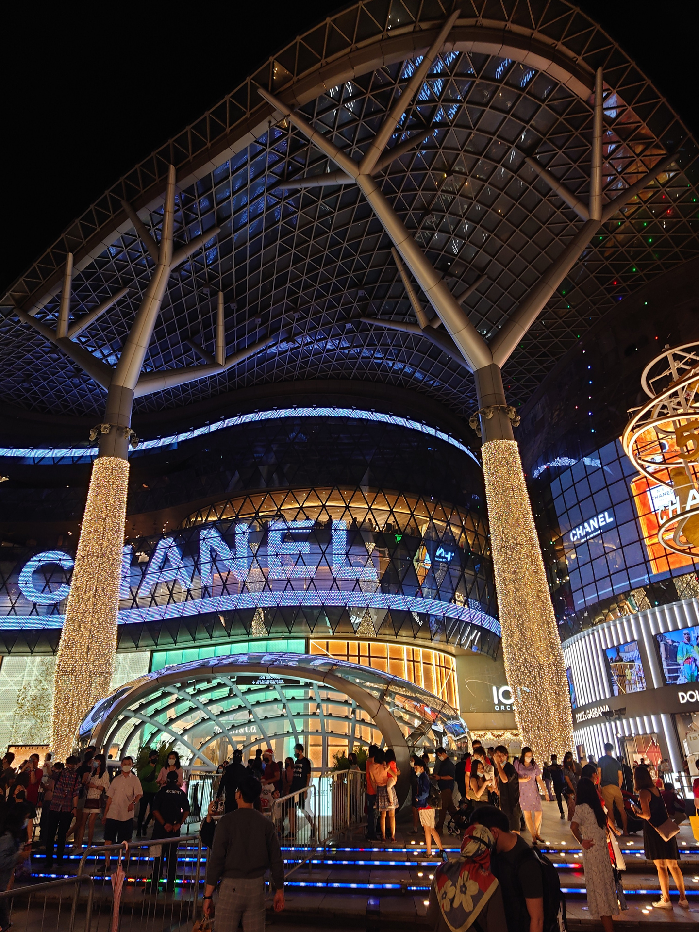 A busy street in front of a big shopping building lit up at night