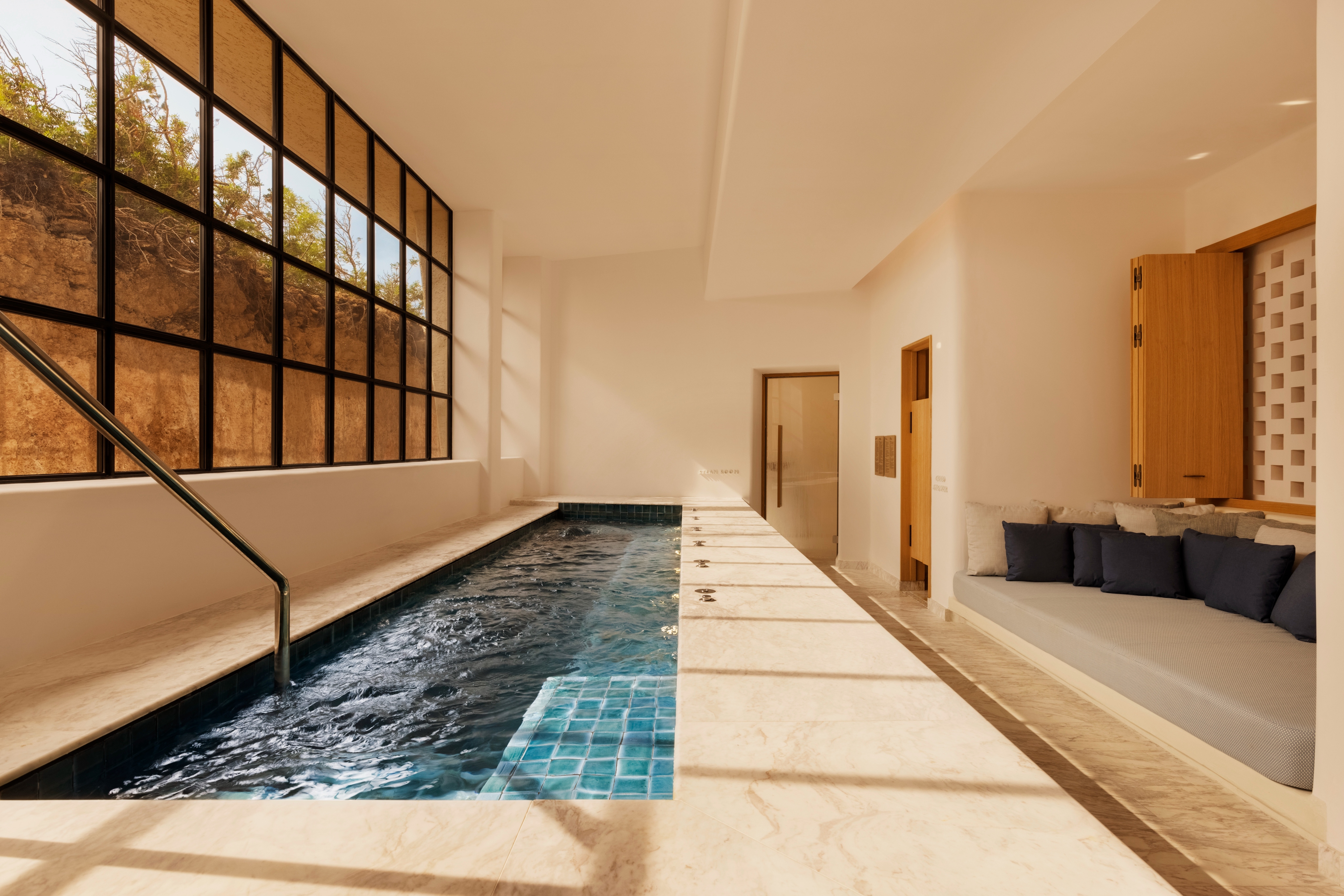 Indoor swimming pool with large windows, seating area, and natural light.