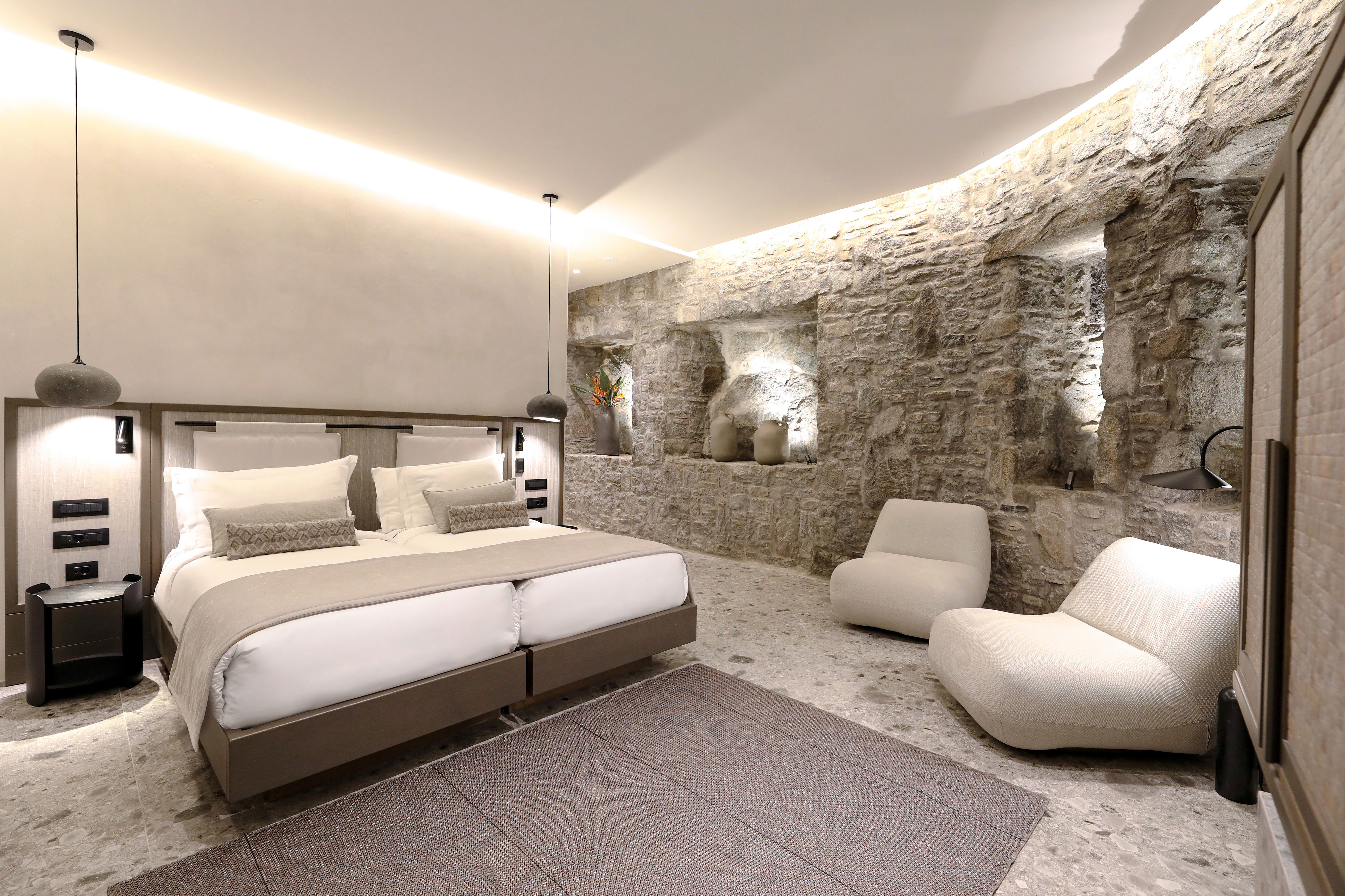 Suite with king bed and curved stone wall feature at Aeonic Suites & Spa
