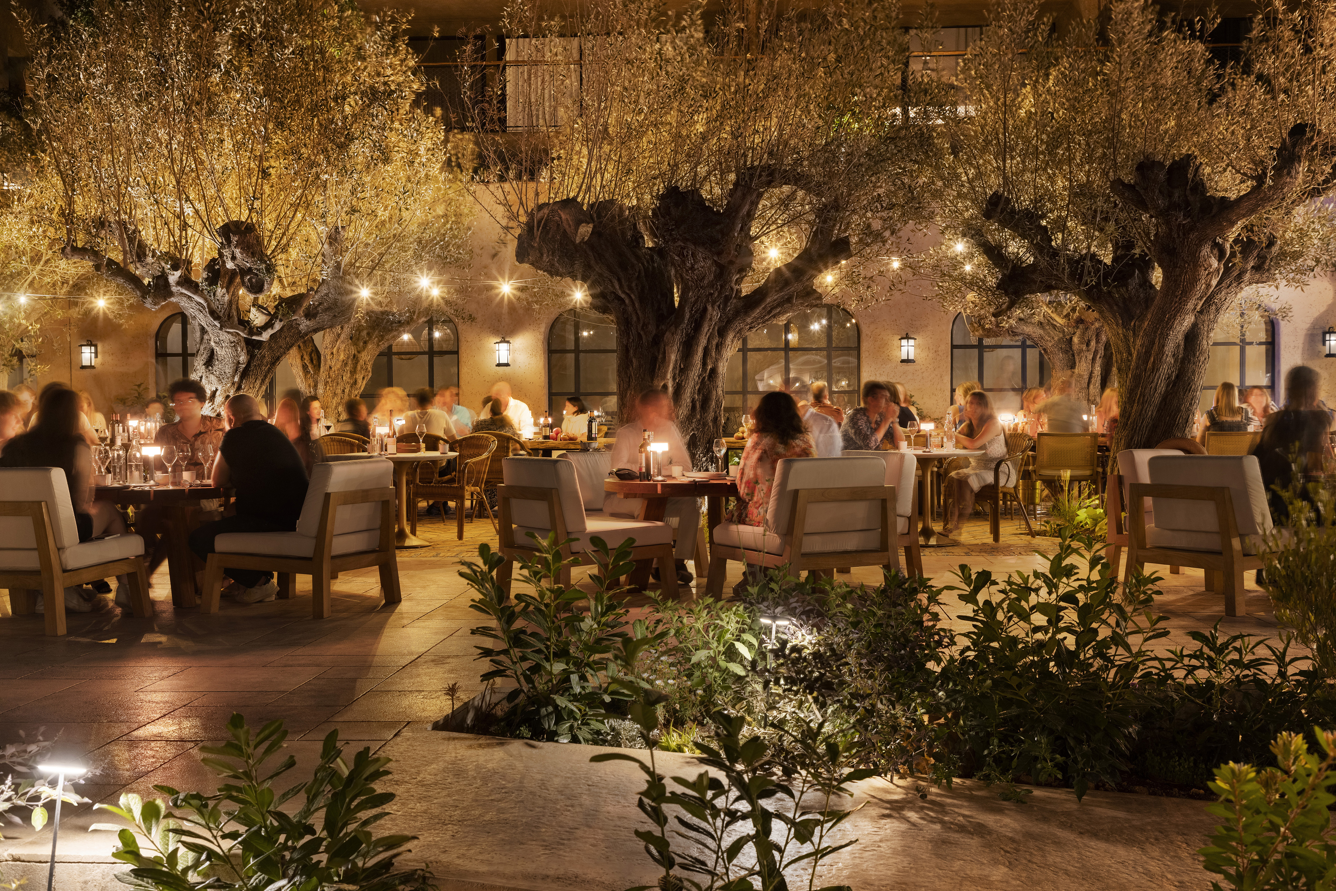 La Plaza at Six Senses Ibiza with people dining at tables beneath olive trees and surrounded by lights at night