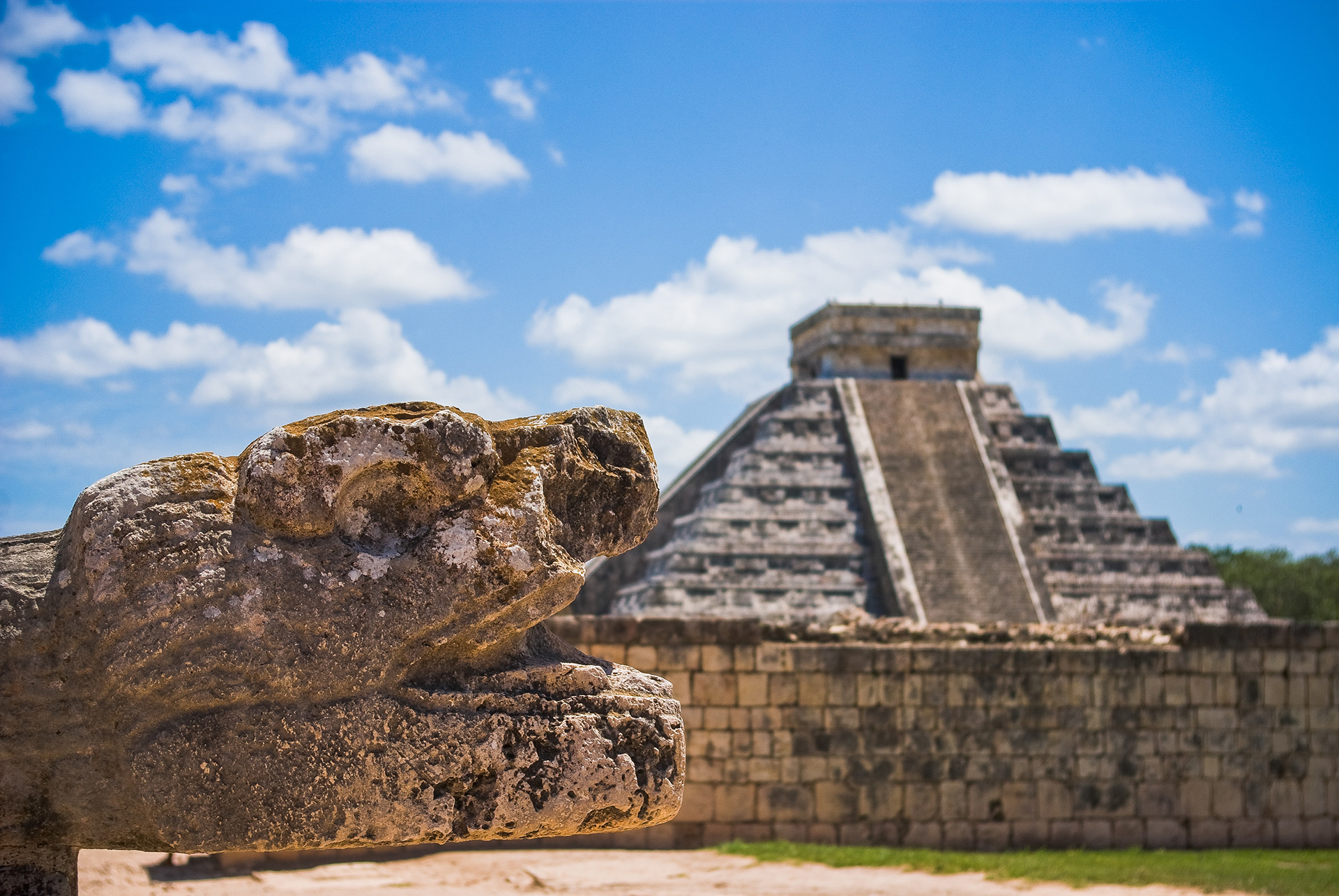 A snake stone head with Chichen Itza in the background
