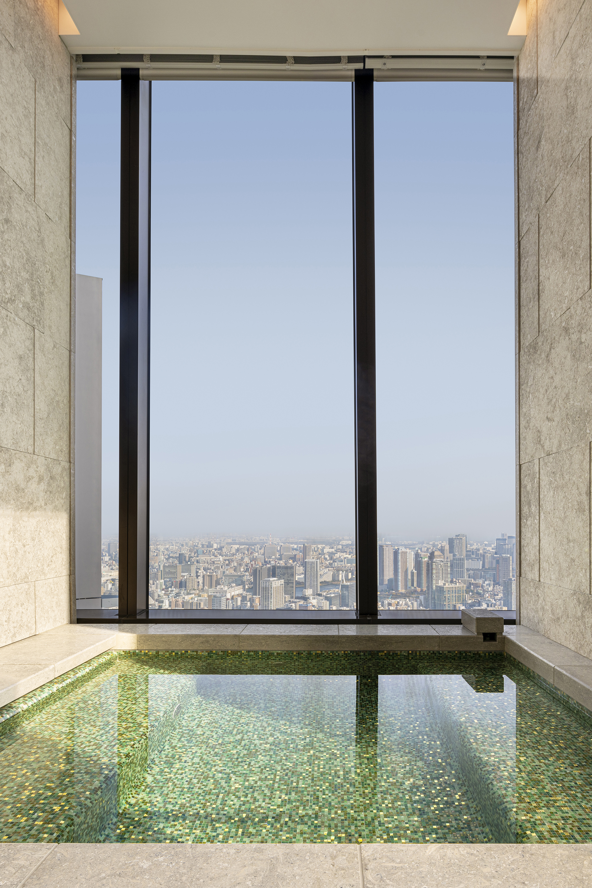 A stone plunge pool in the spa at Bvlgari Tokyo with a floor to ceiling window looking out over the city