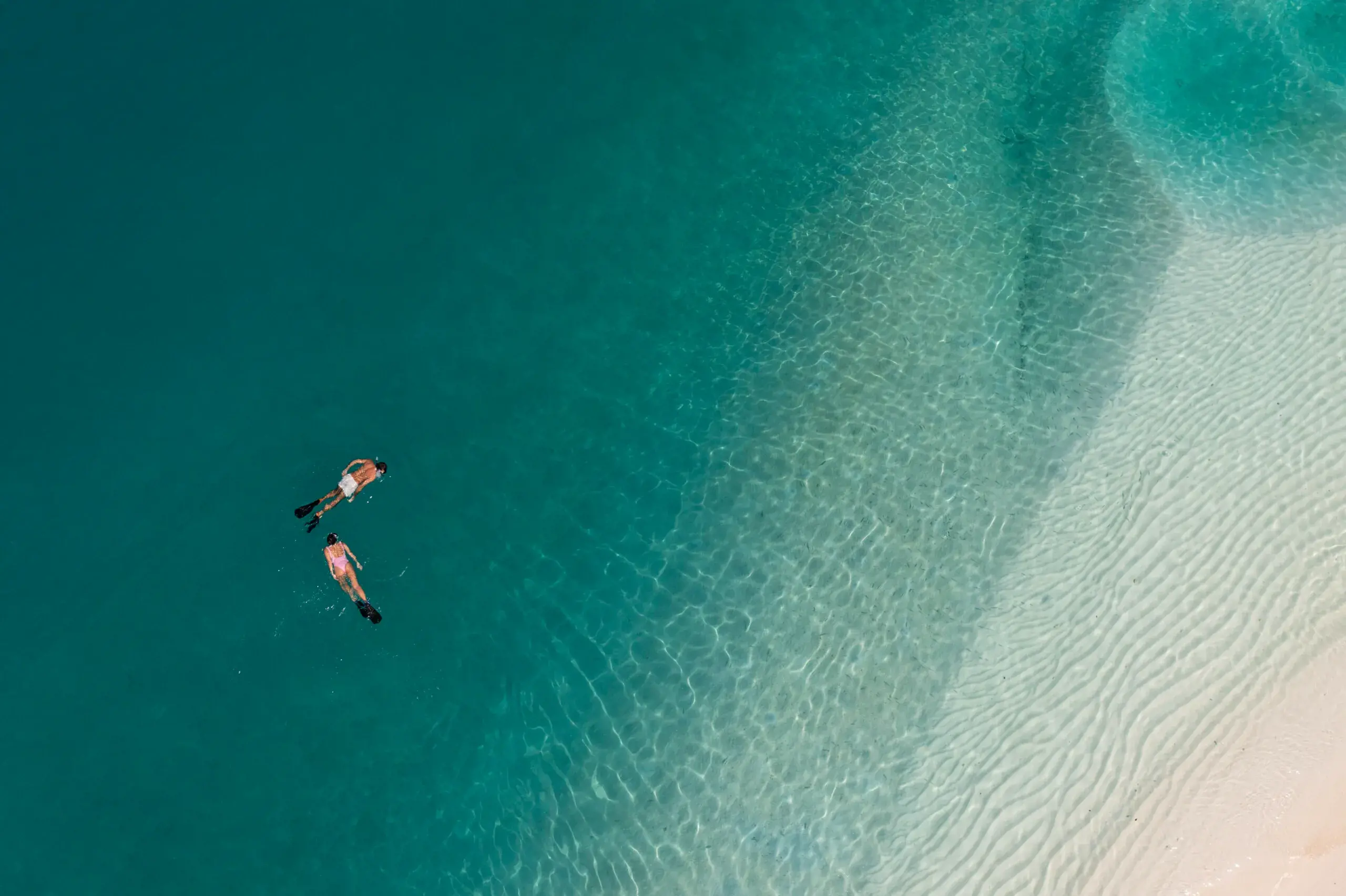 Two people snorkeling in clear turquoise water near a sandy beach.
