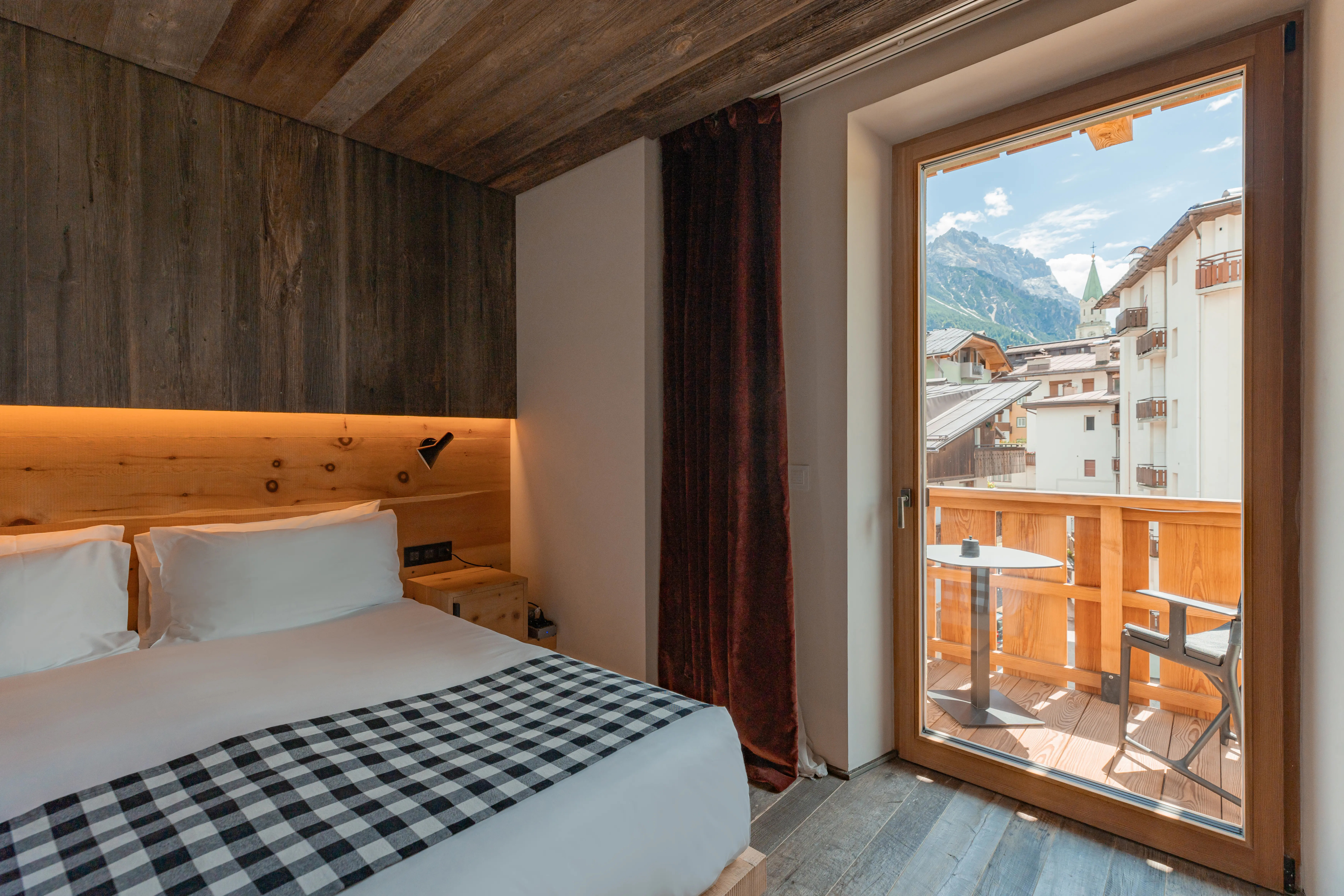 Superior Balcony room featuring bed with checkered throw and large door onto balcony with views of town centre