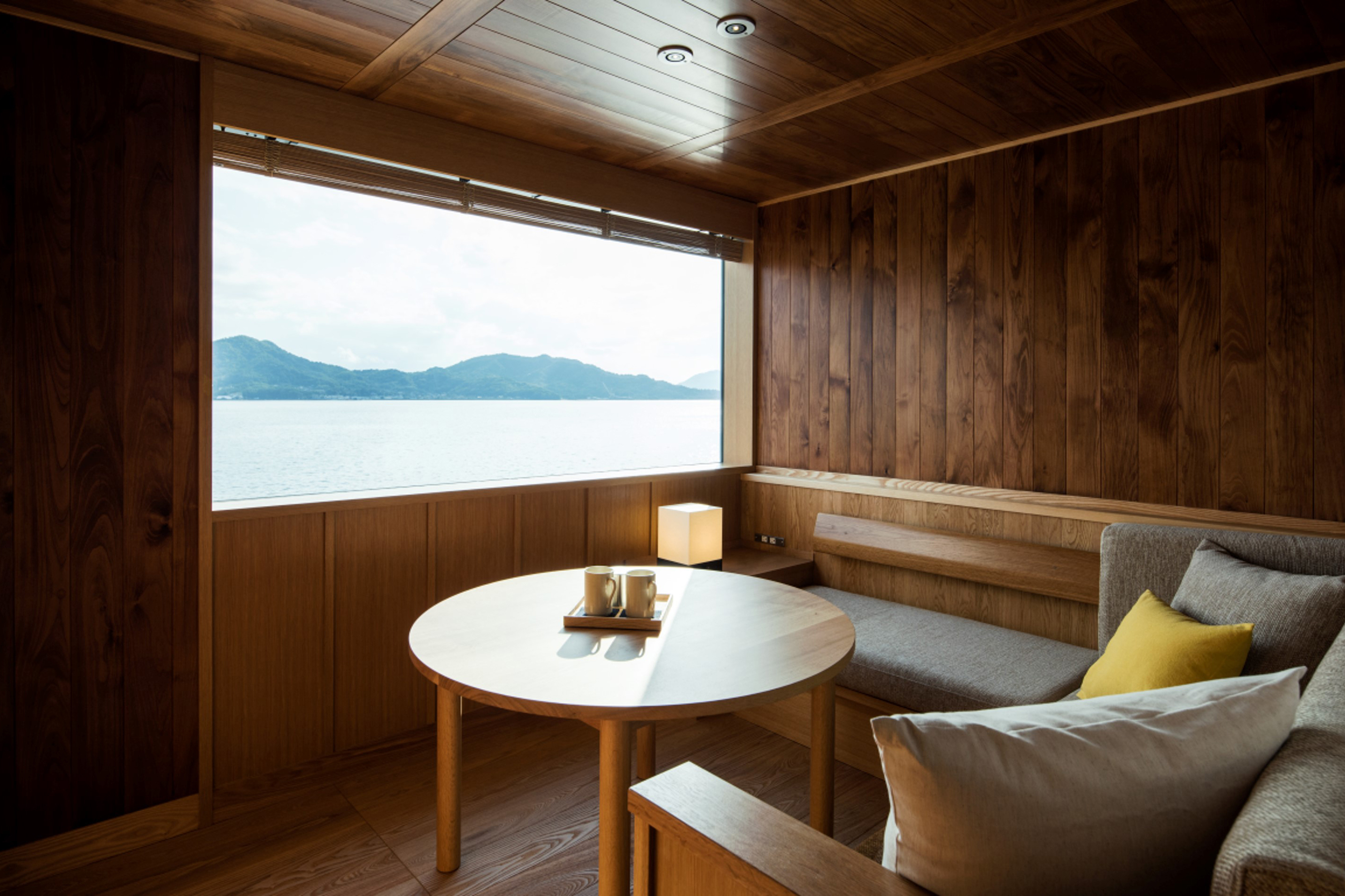 An enclosed seating area with warm wooden furniture and a window looking out over water to mountains