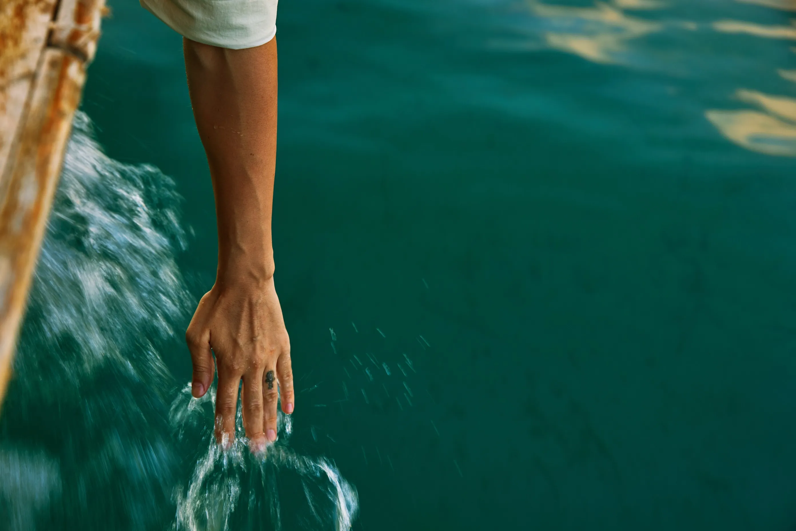 Hand reaching from a boat to touch the water’s surface