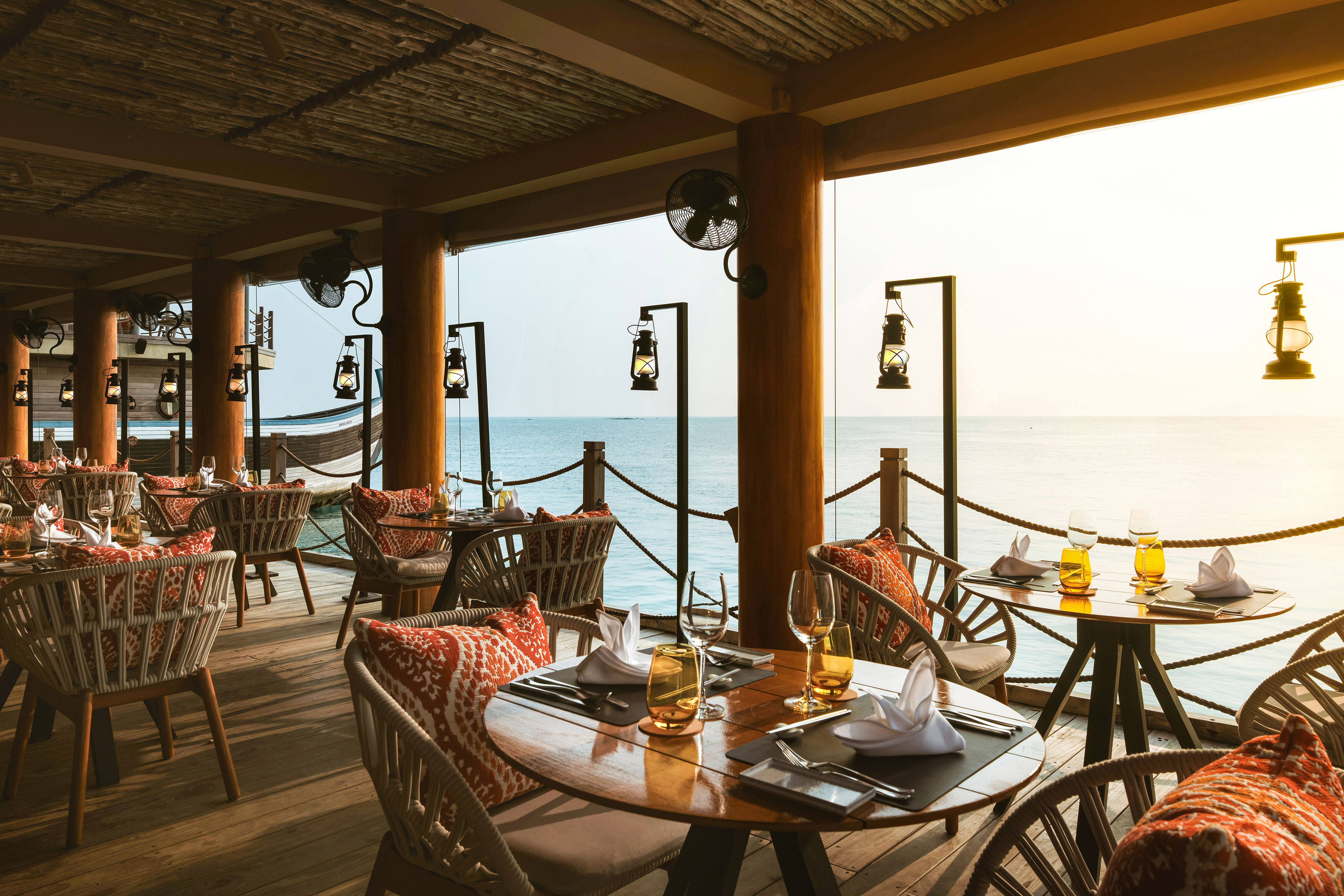 The Fishmarket Restaurant at InterContinental Maldives with ocean view, elegant table settings, and cosy seating beneath a woven ceiling.
