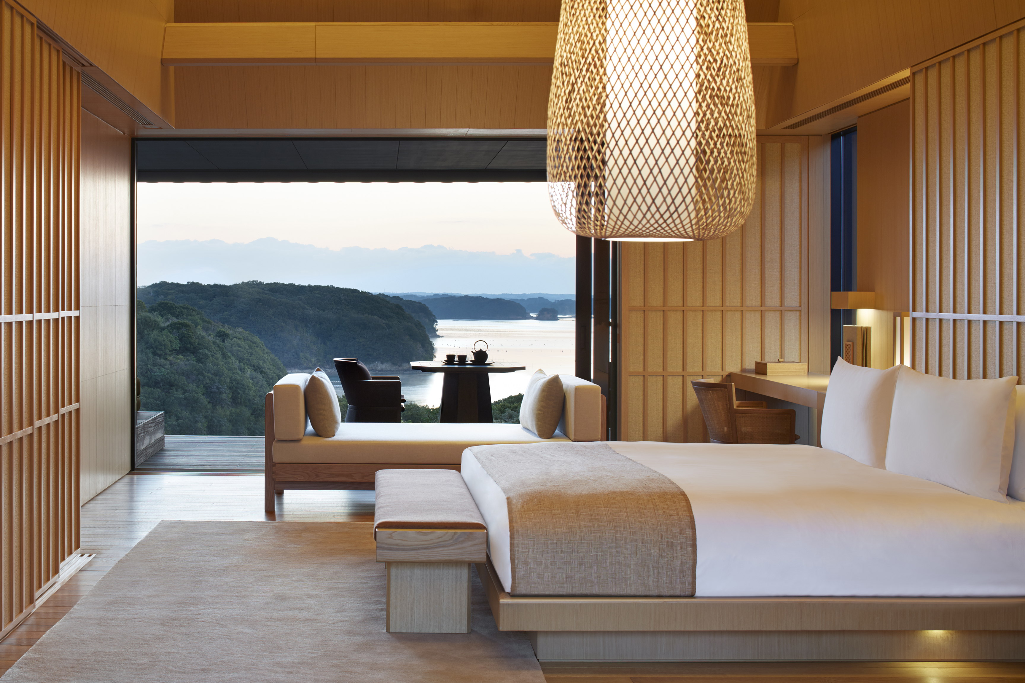 Nagi Villa Bedroom featuring pale wooden furniture and a large window with a view of the mountains and sea
