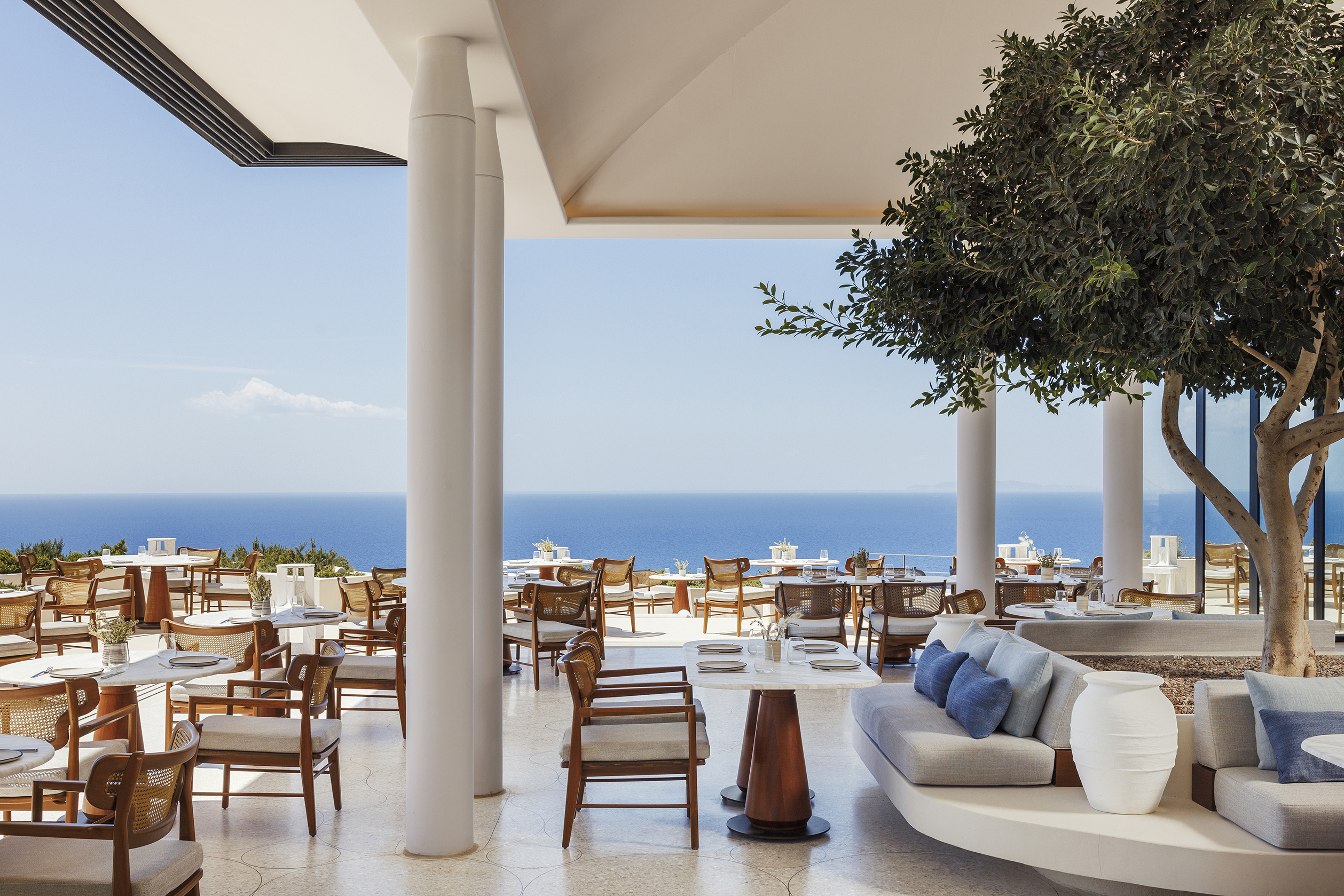 Interior of Atria Restaurant with tables set beneath white columns and established olive tree