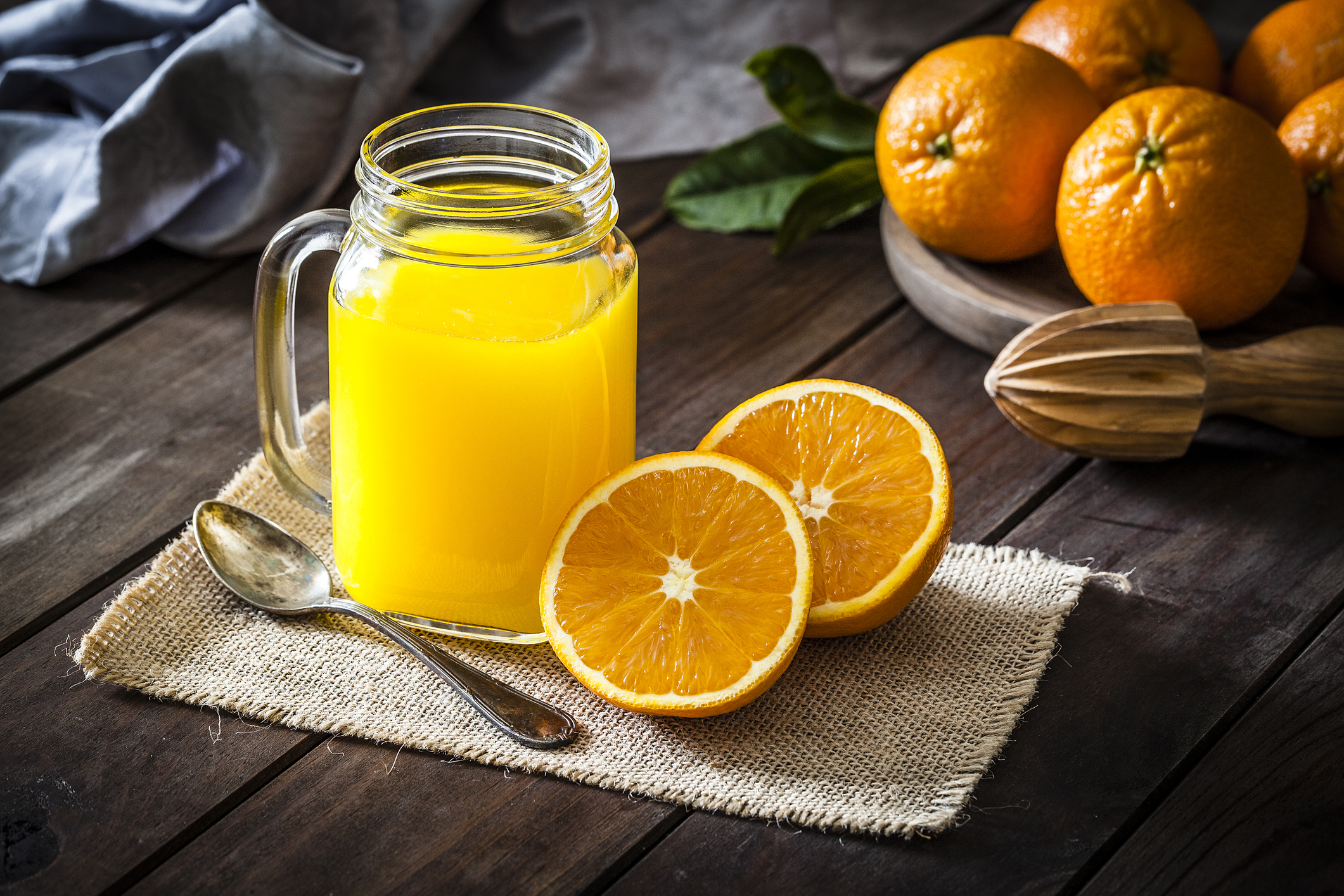 A mason jar filled with orange juice sits beside a bowl of oranges and a hand juicer