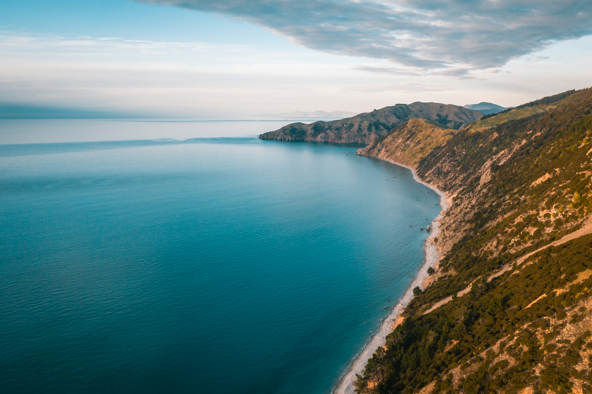 Aerial view of a coastal landscape with a calm blue sea, rugged hills, and a sandy shoreline