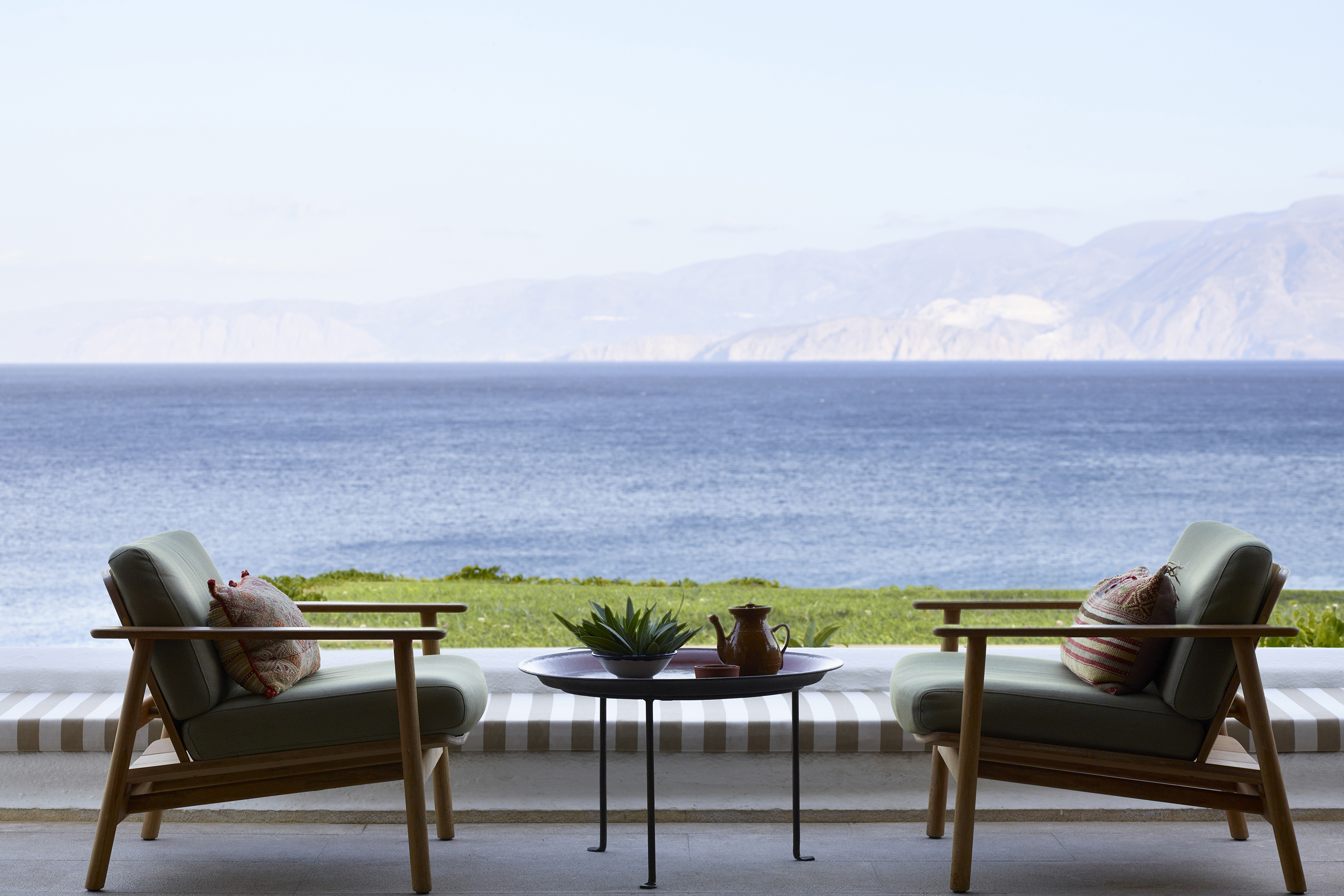 Two comfy chairs of the KAravia Bar facing each other with sea views in the background
