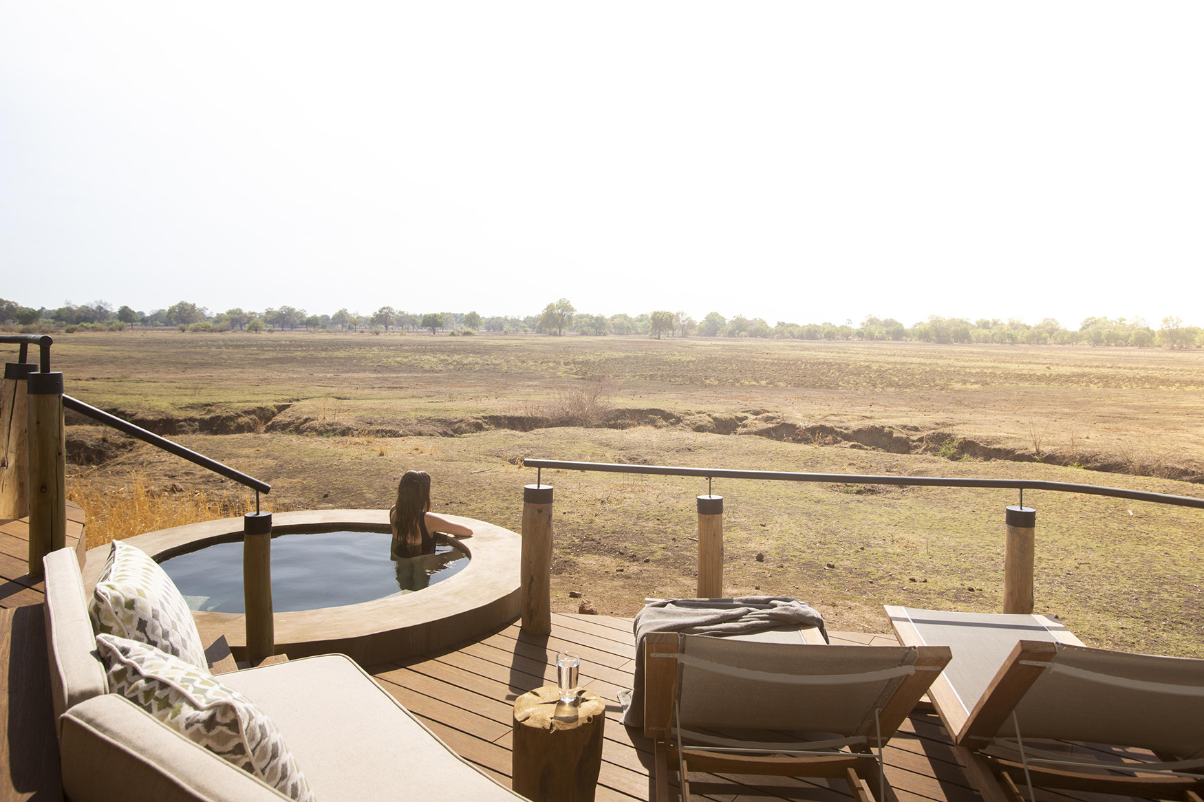 Africa, Zambia, South Luangwa National Park, Puku Ridge Camp, private terrace with sunloungers and woman in private pool looking out over landscape