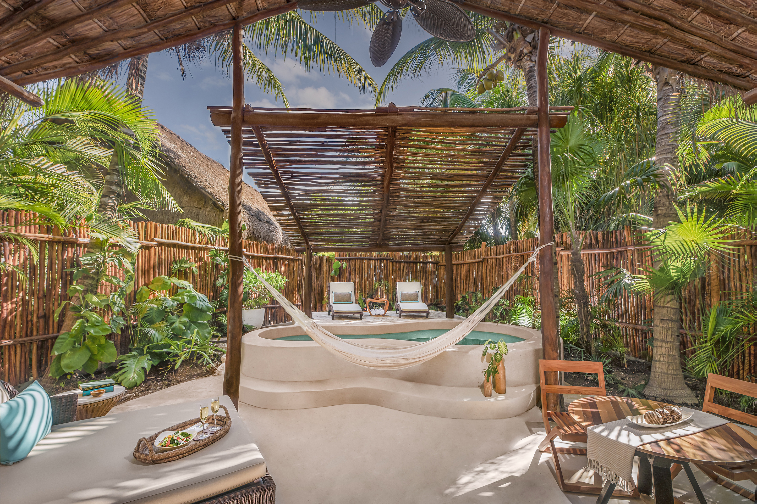 A rustic-chic suite garden featuring a private plunge pool and loungers beneath a woven canopy, a hammock, bistro table and woven fence