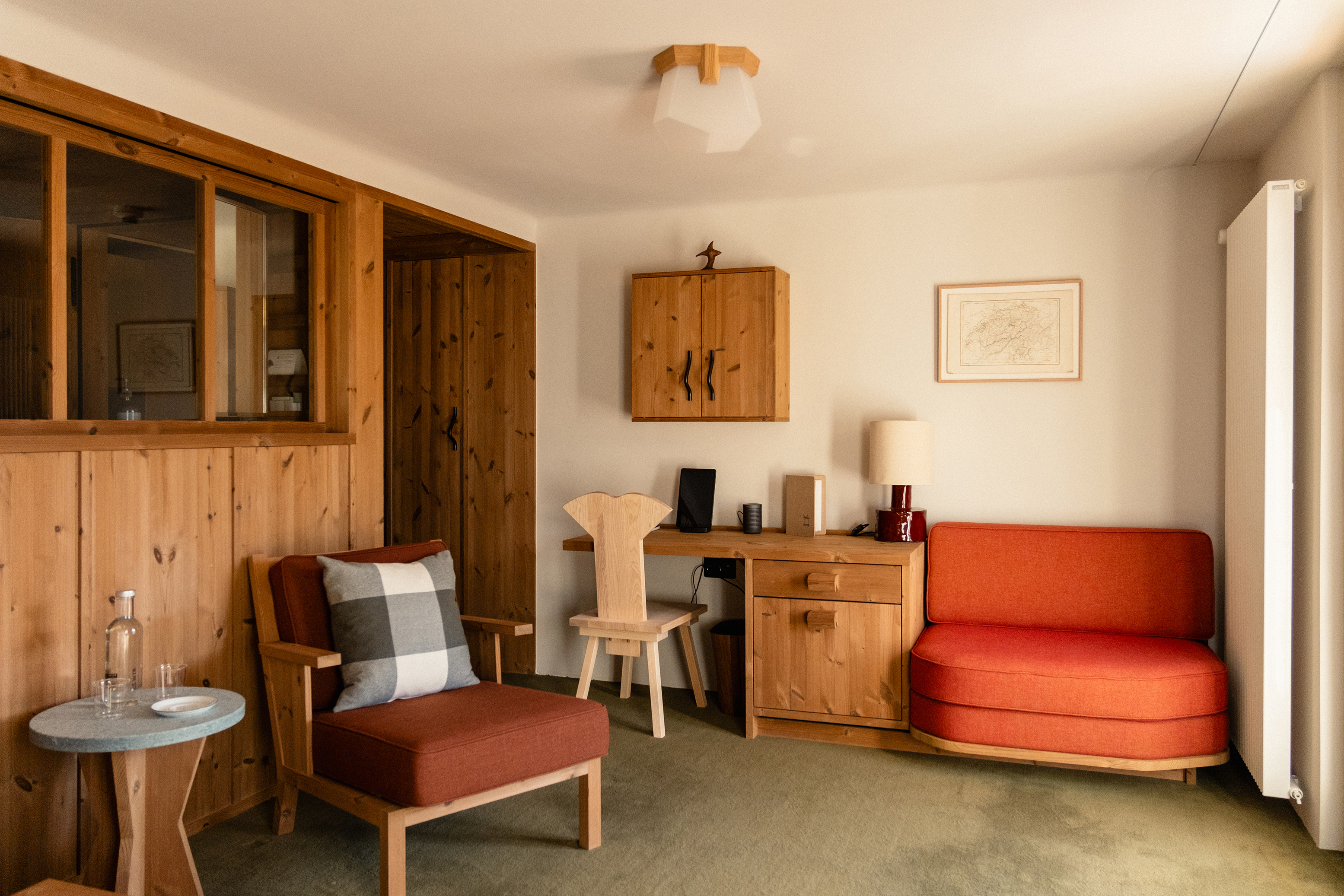 The cosy lounge area of a Deluxe Suite at Grand Hotel Belvedere featuring a small sofa, desk area, table and chair in check and warm tones and wooden panelling on the walls