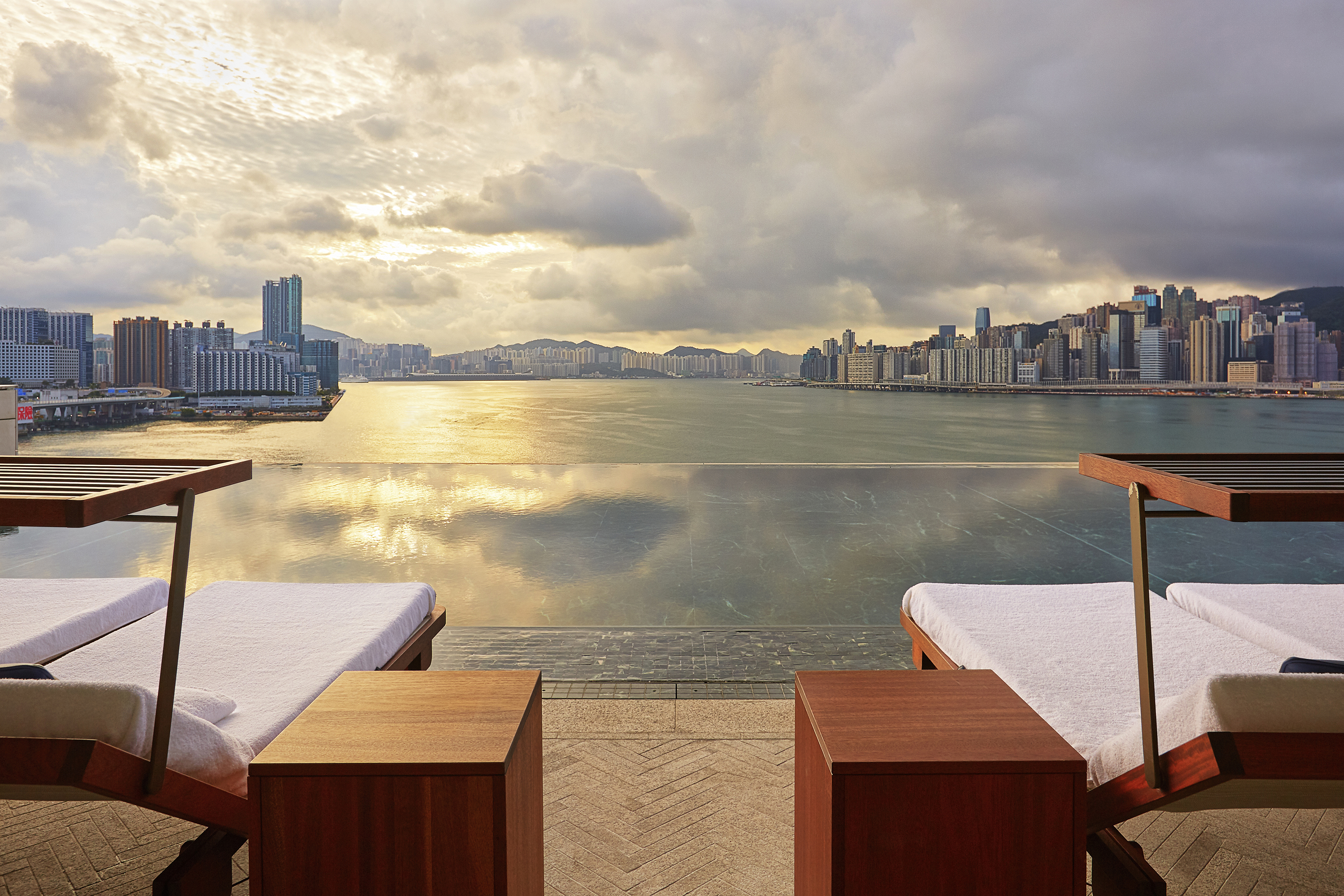 Stylish wooden sun loungers facing the infinity pool at Rosewood Hong Kong overlooking the harbour and city skyline