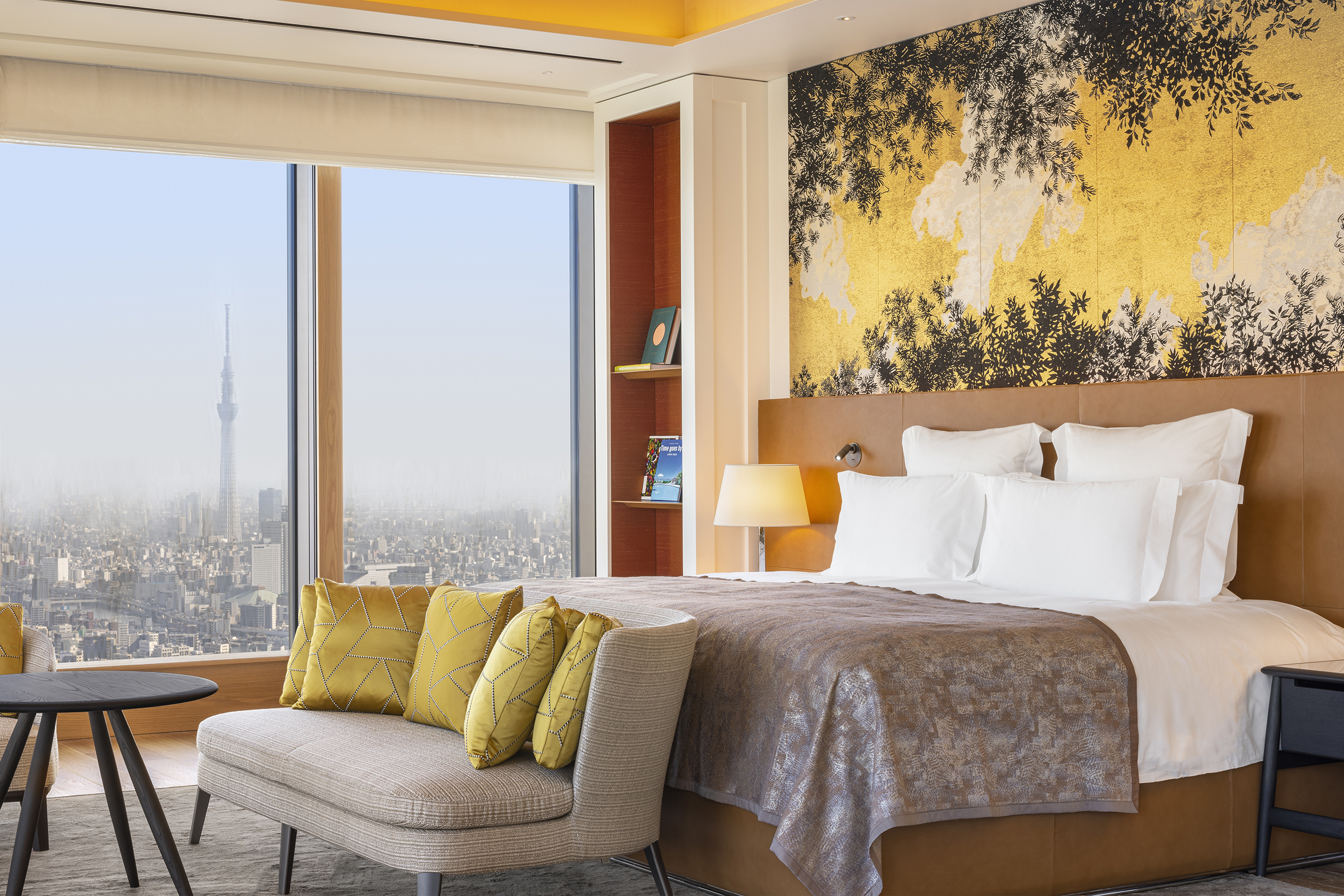 The primary bedroom of the Bulgari Suite featuring a plush bed, ornate wallpaper and comfy seating area with skyline views