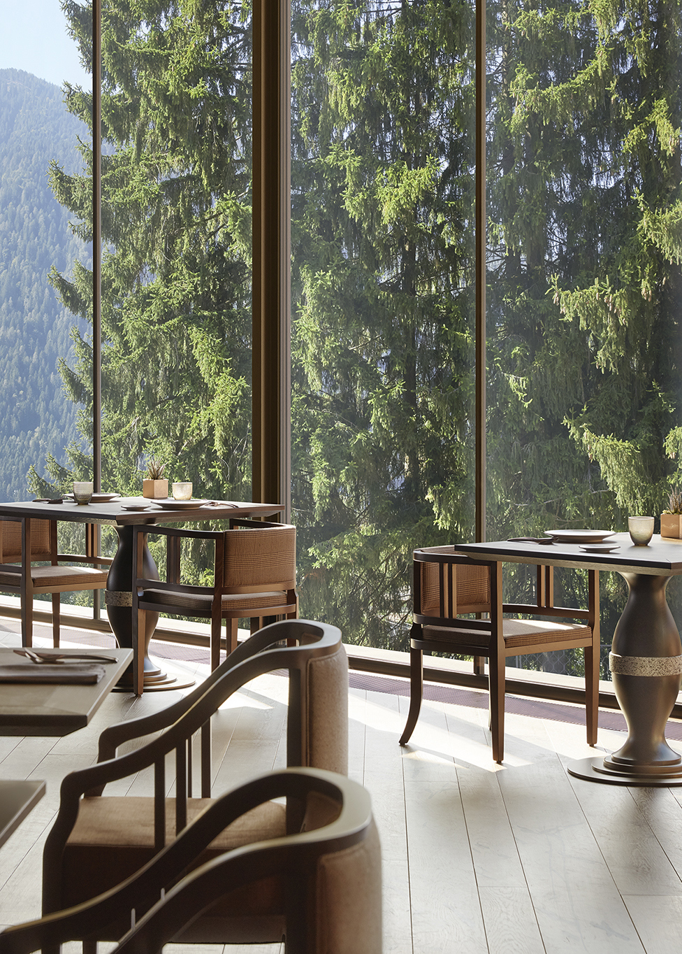 Tables inside Dolomia restaurant set for dinner with views of pine trees glowing in the summer sun