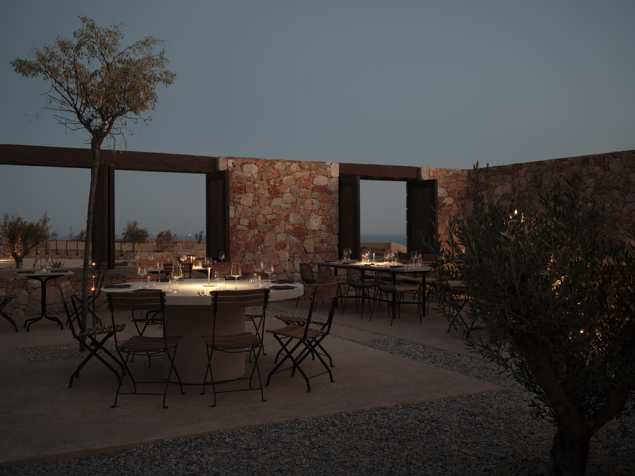 An open air dining area within stone walls featuring two tables set for dinner lit by atmospheric lamps