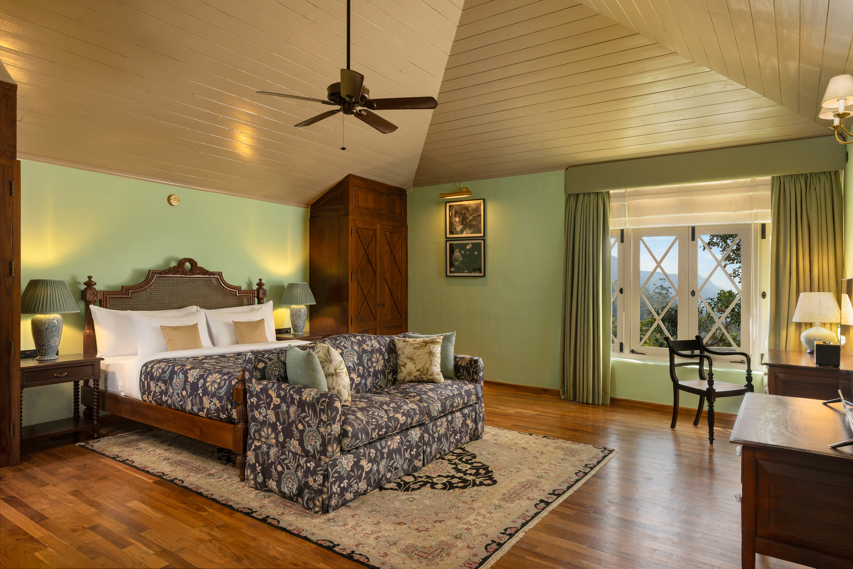 A Planter's Suite at Uga Halloowella with a comfy bed and sofa in a floral design, high panelled ceilings, and dark wood furniture