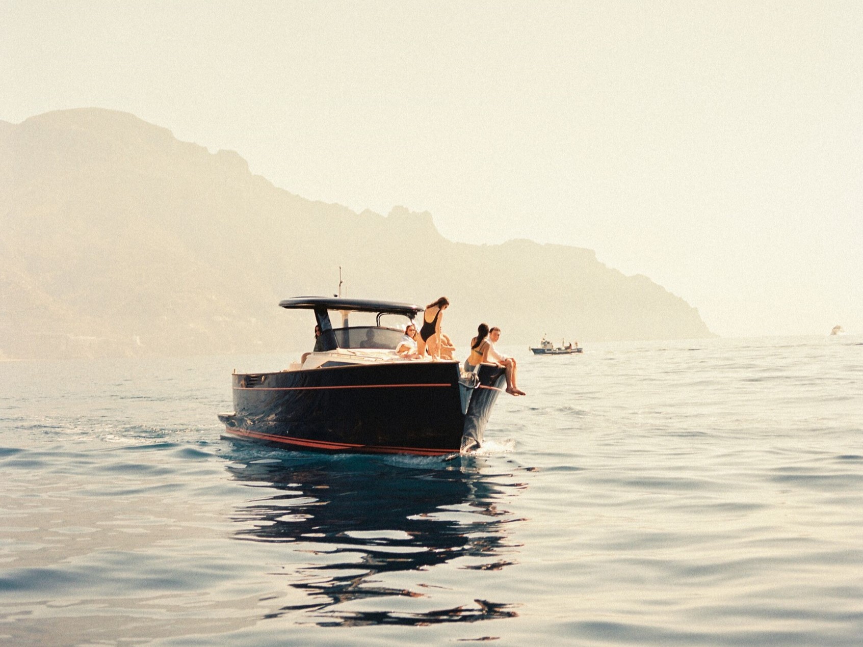 Group of people relaxing on a motorboat in calm waters with mountains in the background