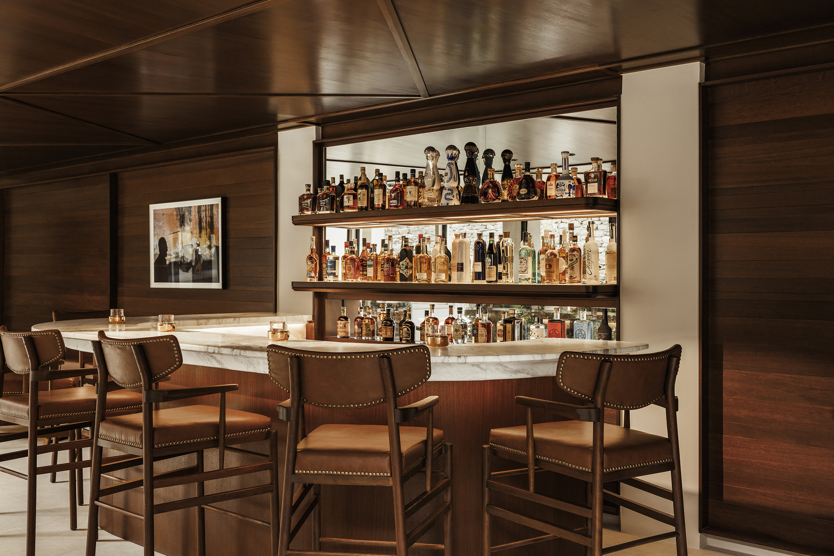 Warm wooden bar in Incognito Lounge with plush bar chairs and mirrored shelves lined with bottles 