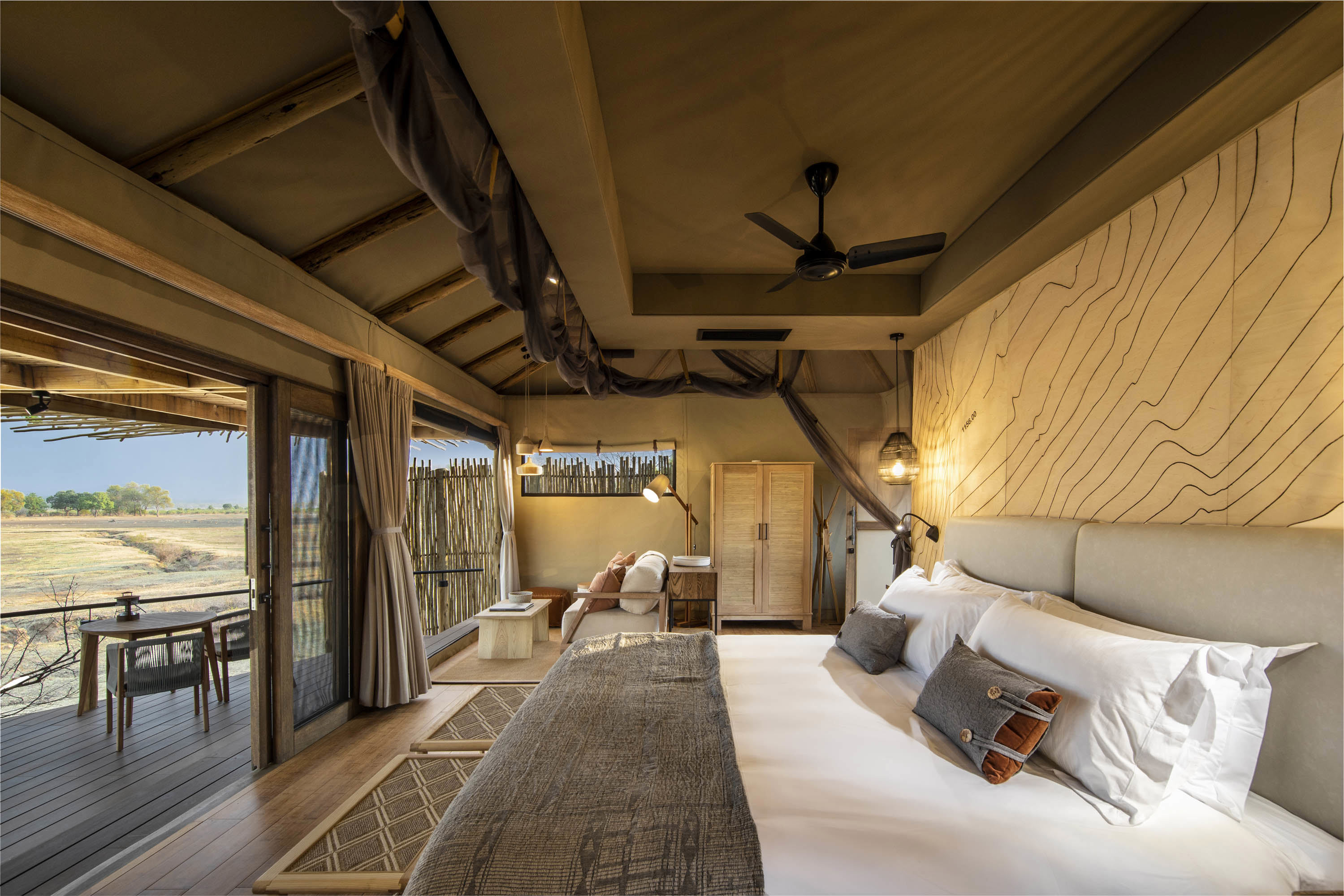 A luxurious safari tent bedroom at Puku Ridge Camp with a large bed, modern decor, and an open view of the surrounding landscape through glass doors leading to a wooden deck