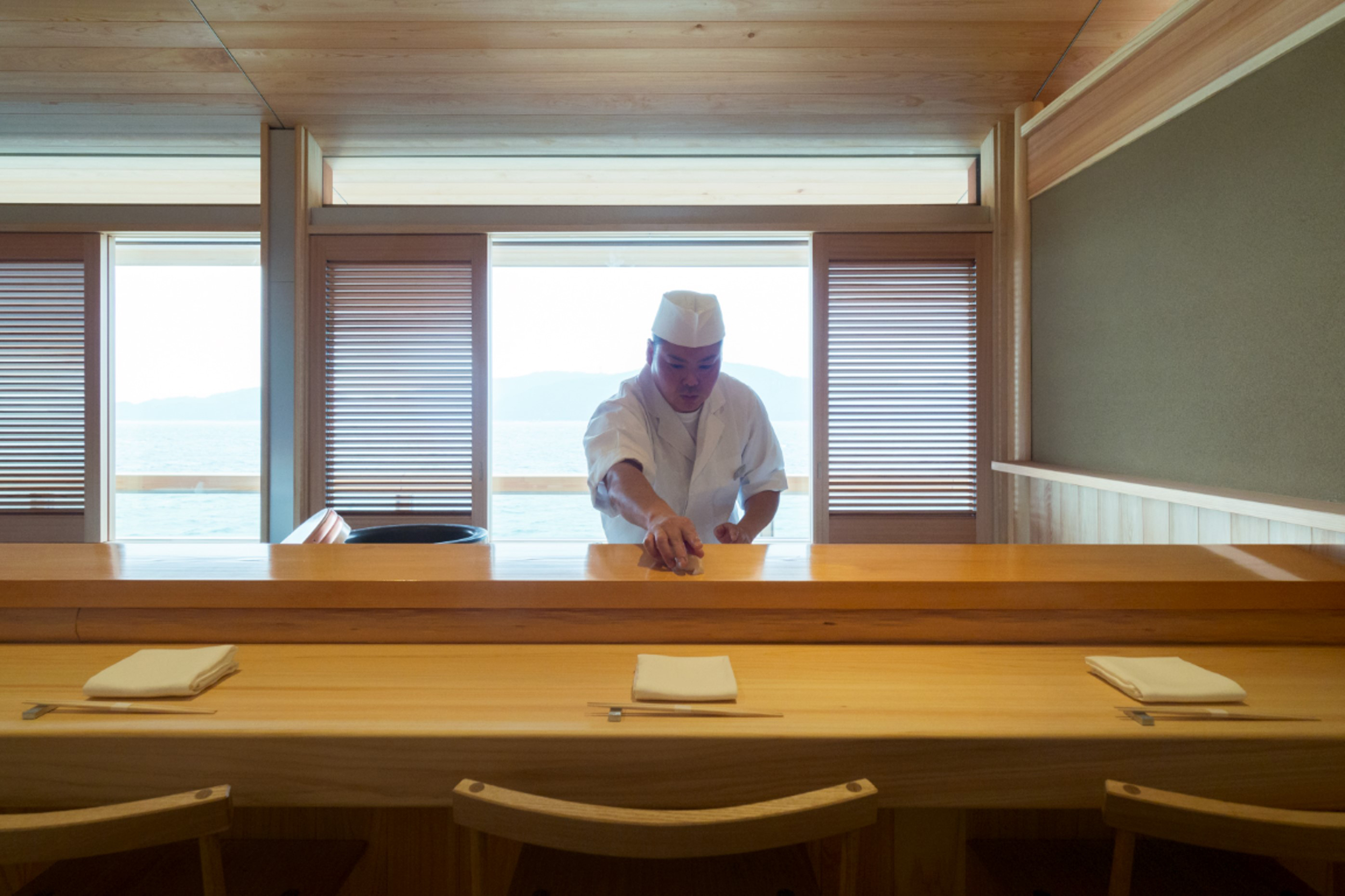 A chef preparing some food in front of three seats set for dining