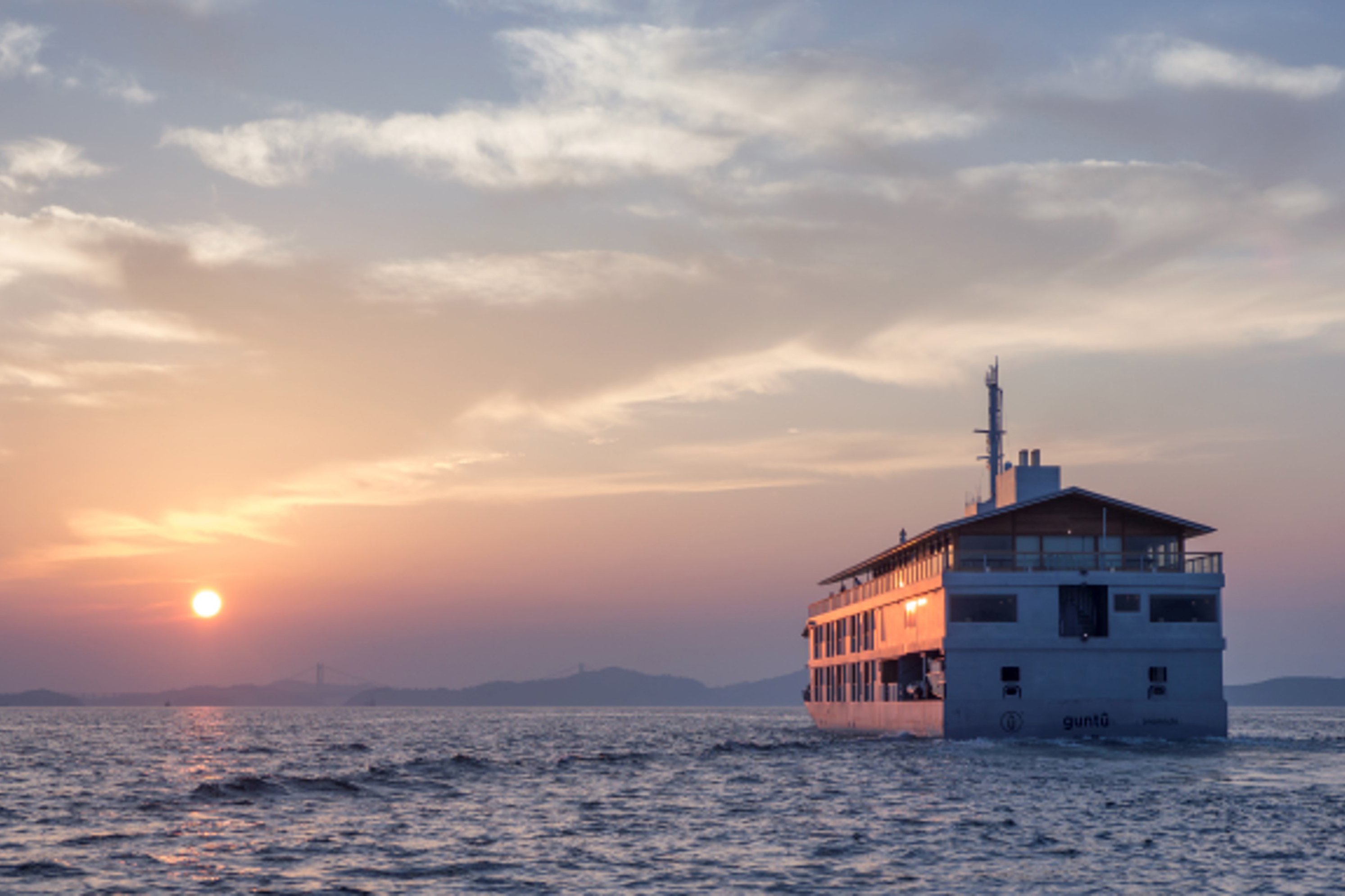 The Guntu boat sailing along calm water into the sunset