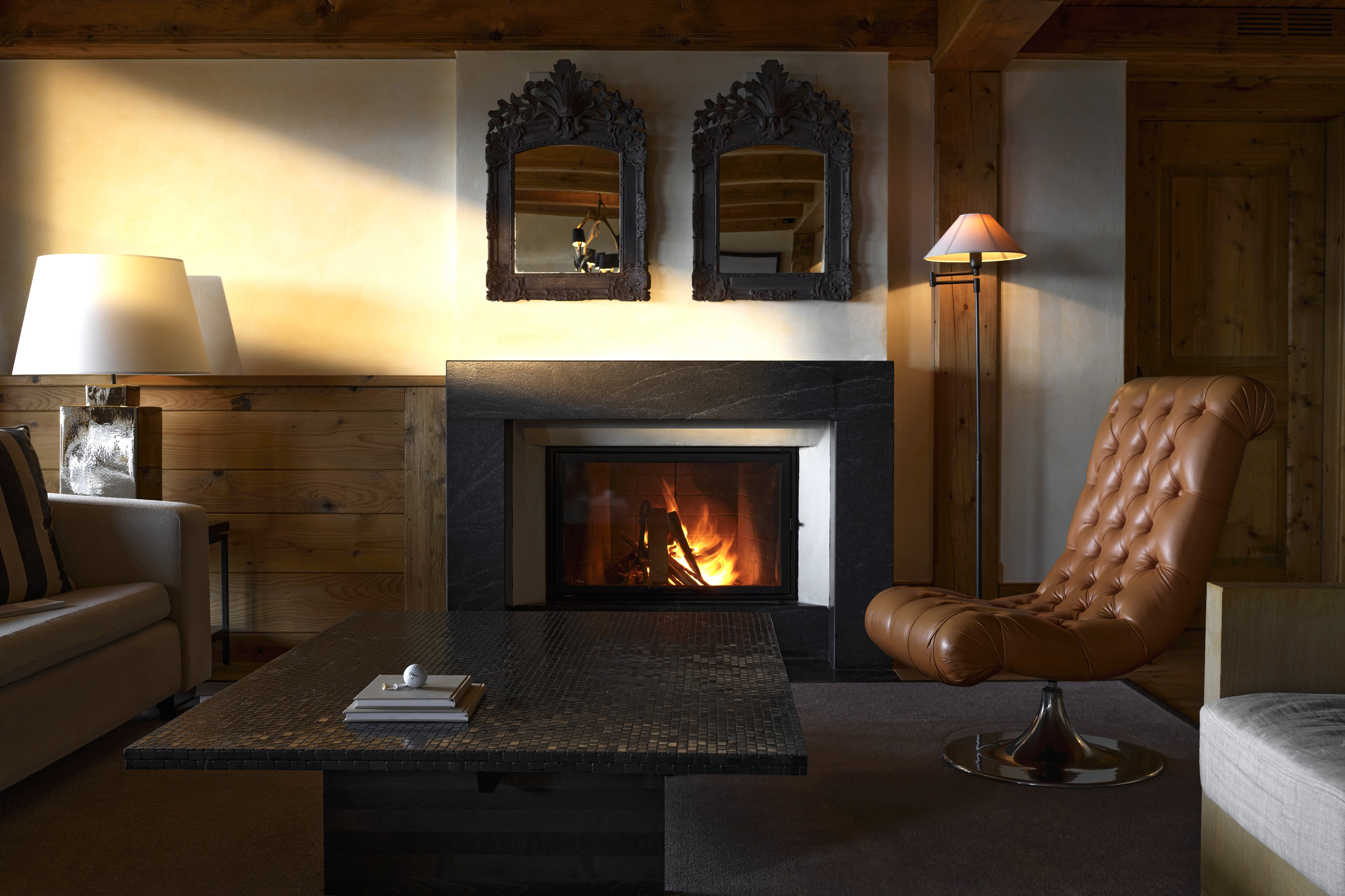 A cosy lounge of an apartment at LeCrans featuring a large coffee table, comfy leather chair and fireplace with two mirrors