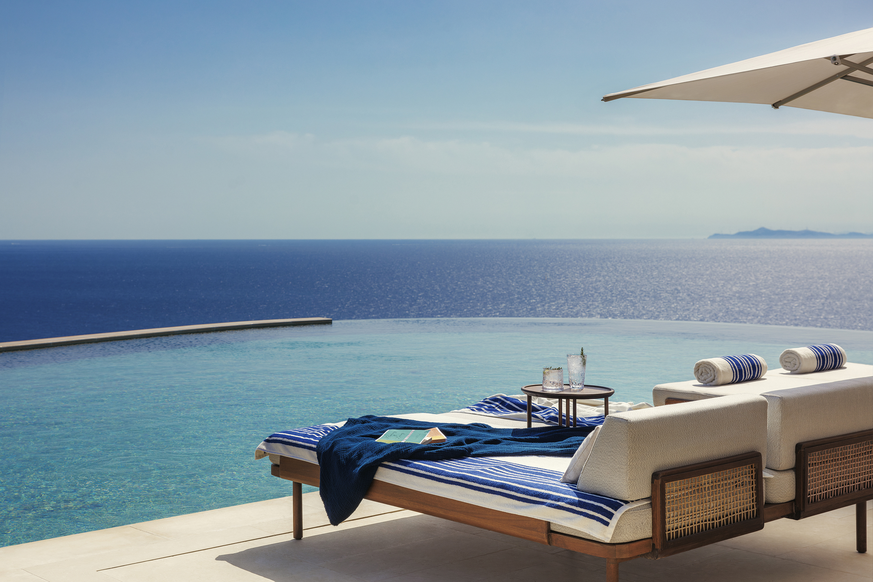 Two rattan pool loungers looking out to sea over an infinity pool