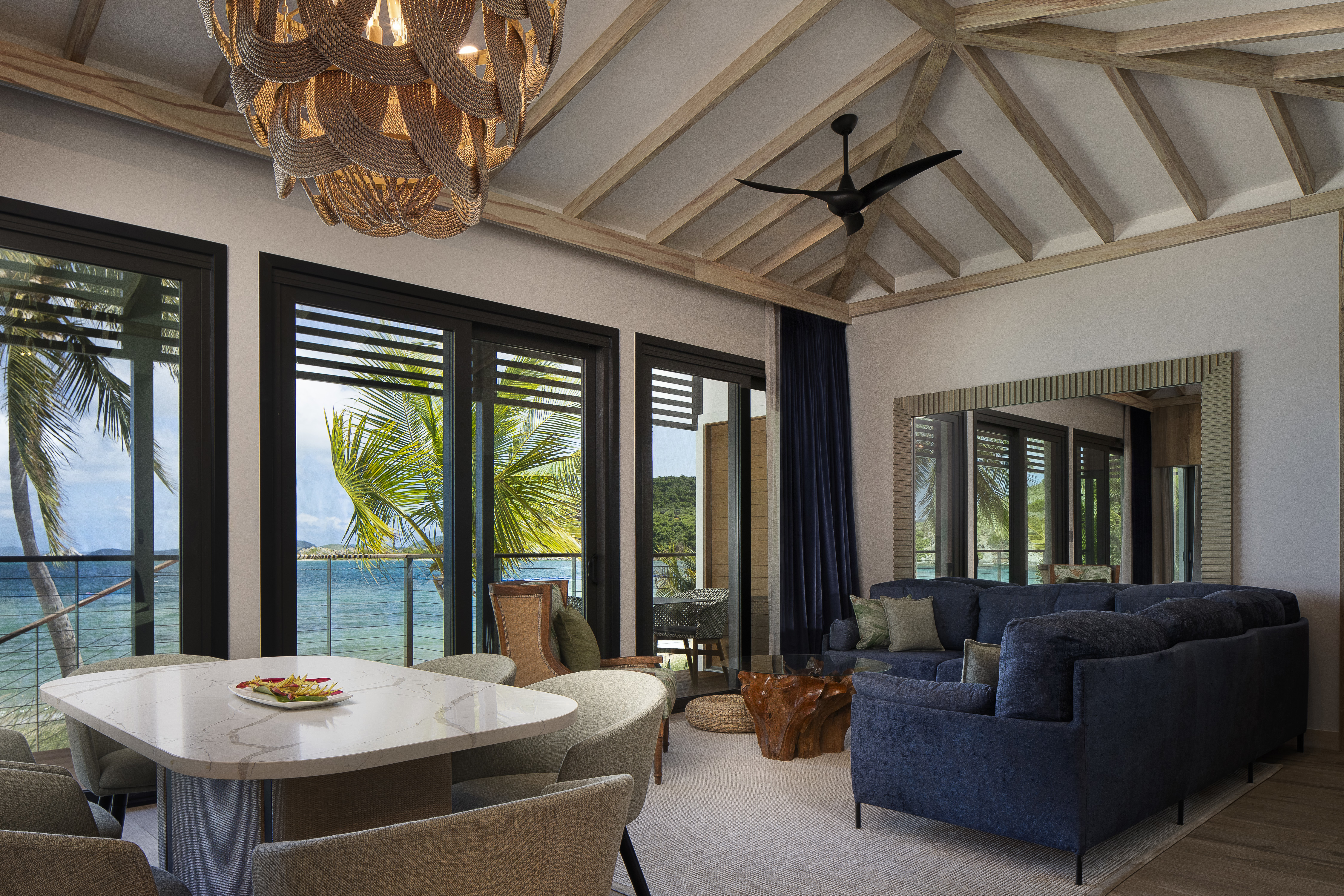 Plush villa lounge with seating area and dining table below a beamed ceiling with wooden chandelier and large sliding doors