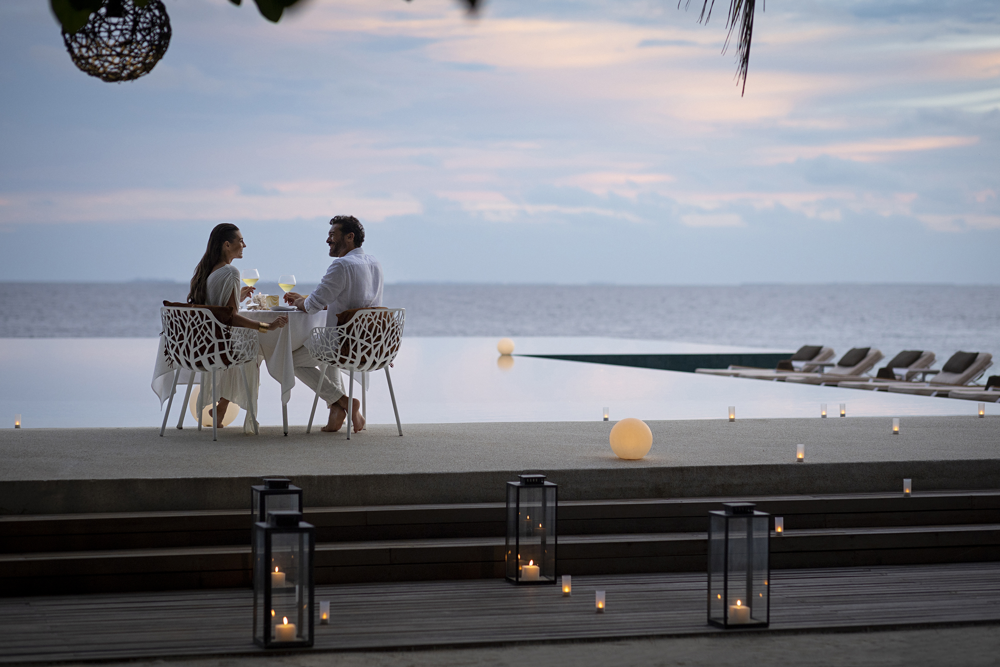 A couple sat by the pool surrounded by candles at sunset during a private dining dinner