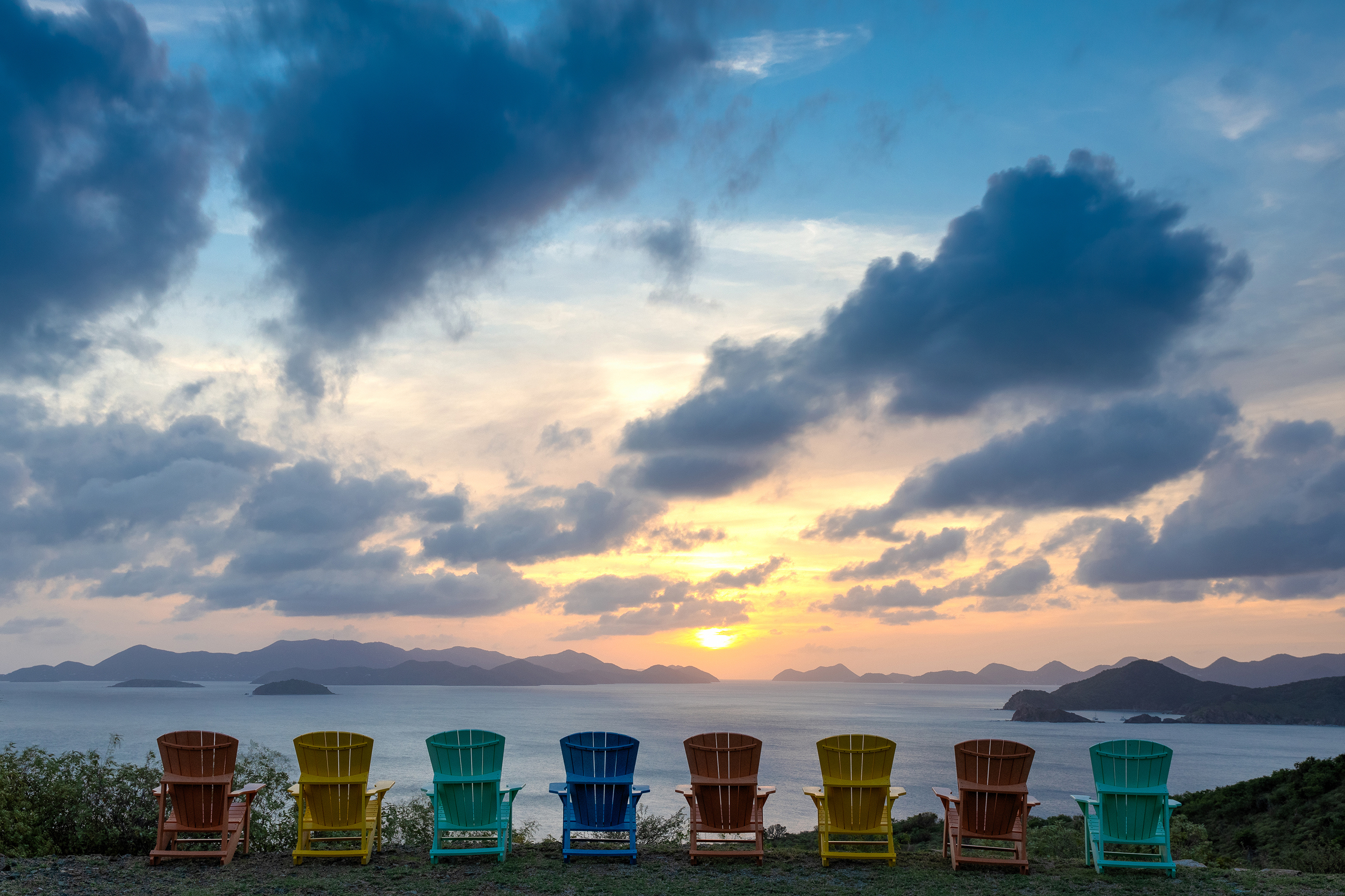 Colourful wooden deck chairs lined up facing the setting sun over the ocean