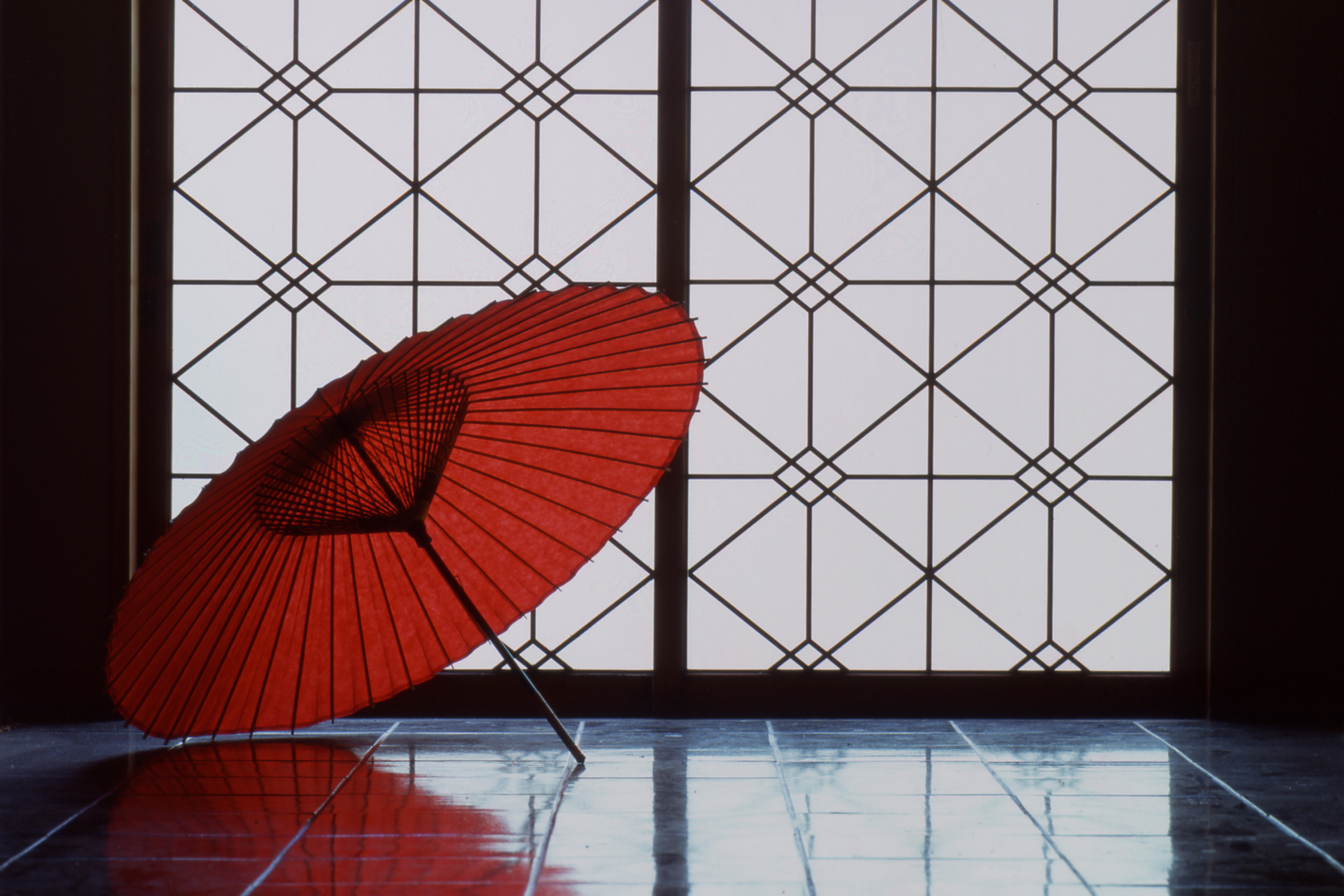 An open red Japanese umbrella on the floor in front of an ornate wall