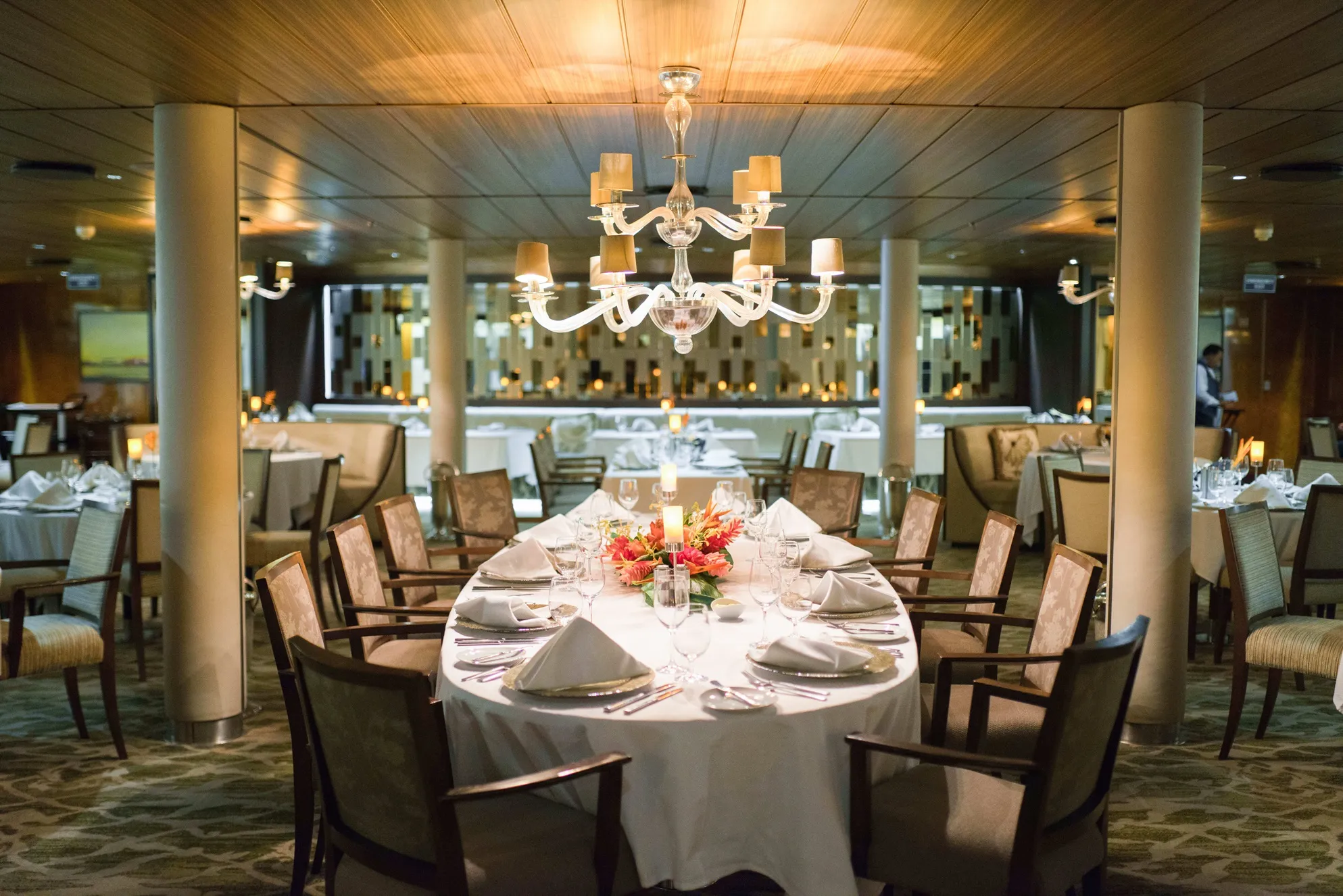 An elegantly set dining table with a floral centerpiece in a sophisticated restaurant, lit by a chandelier.