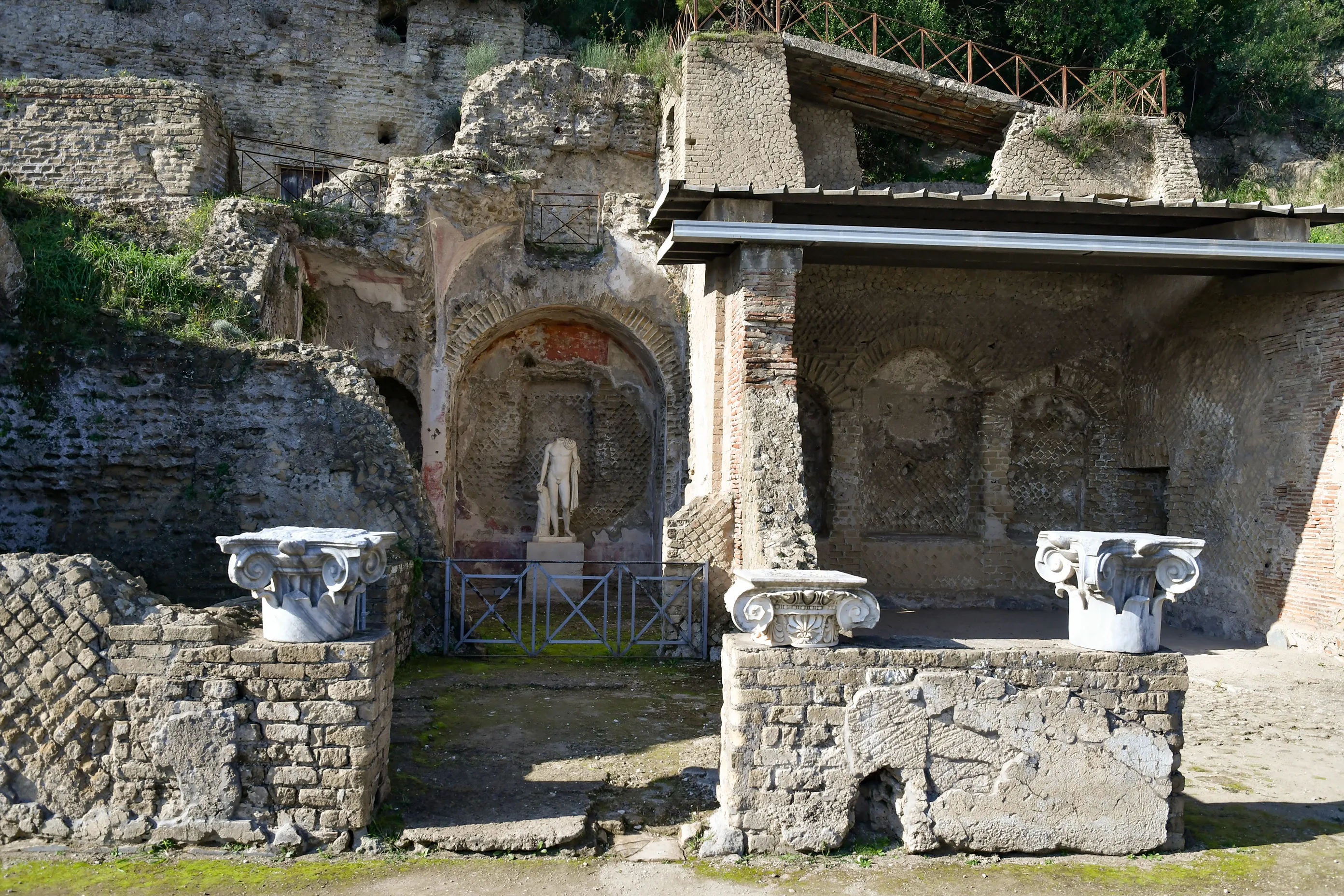 Ancient Roman ruins with stone walls, arches, and a marble statue at the archaeological site of Baiae in Italy.