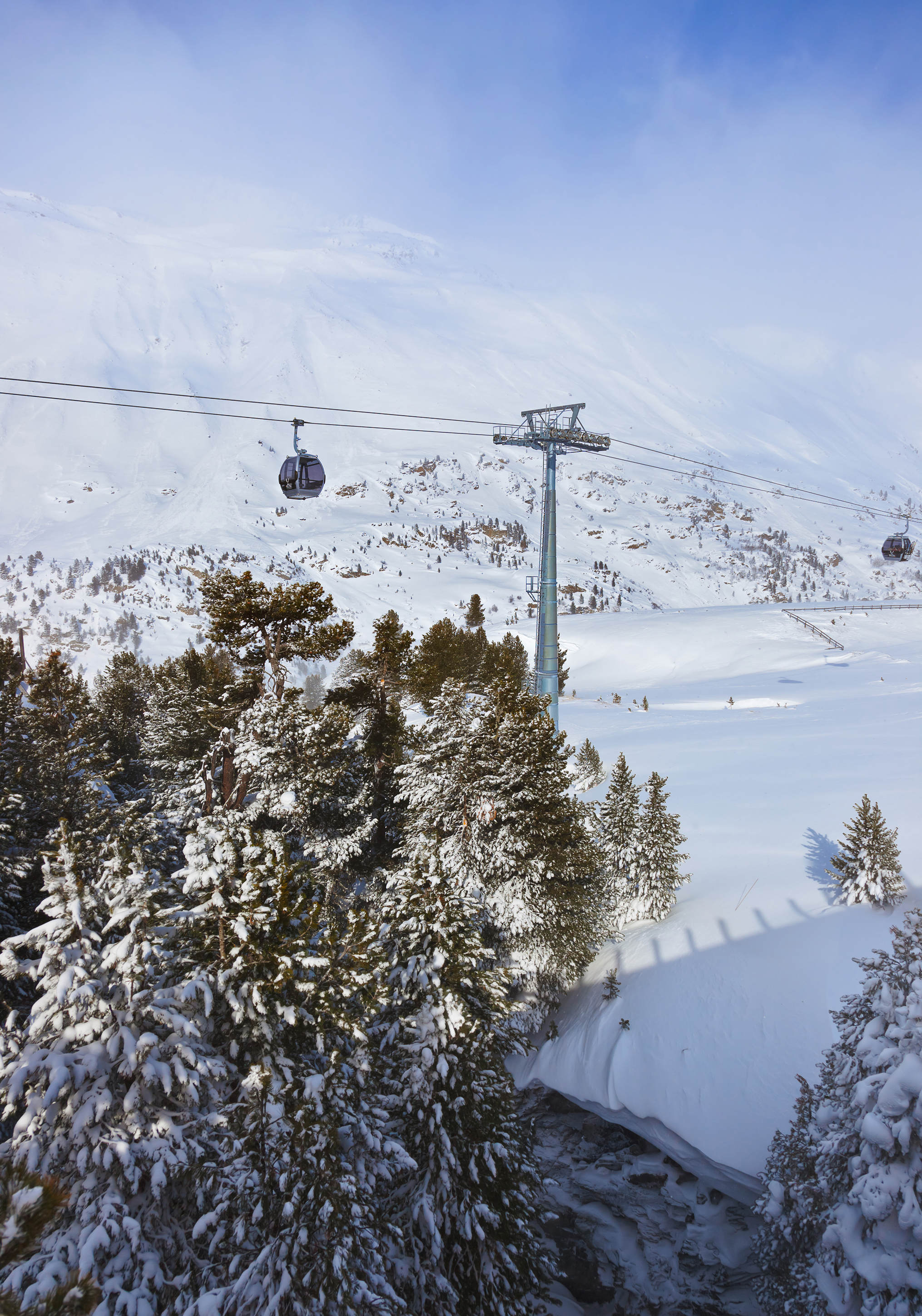 Scenic winter landscape of Obergurgl, Austria with snow-covered trees and a gondola lift against a backdrop of snowy mountains.