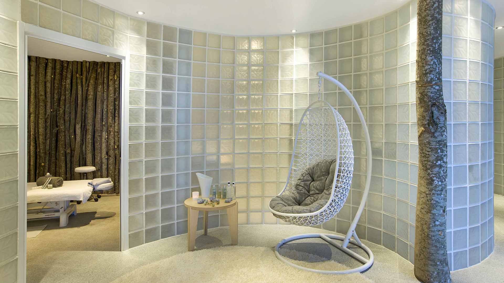 A chic spa in the Altapura hotel, spa beds and a luxe chair are in a room decorated with frosted glass