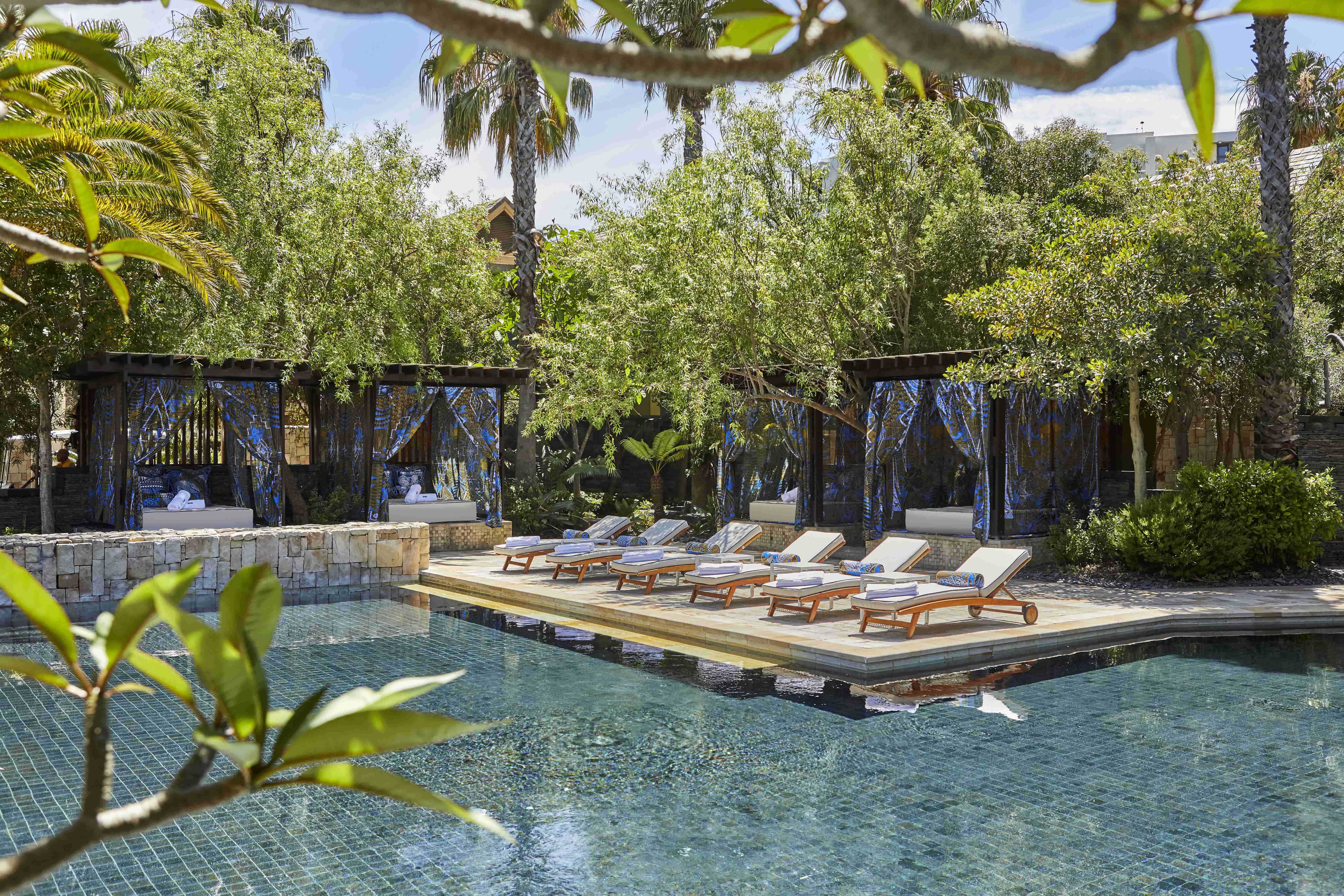 A picturesque pool framed by palm trees and lined with loungers and cabanas at One&Only Cape Town