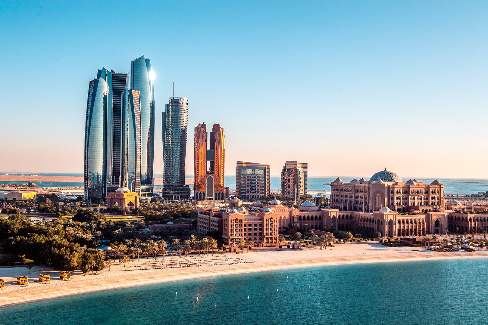 A skyline view of modern skyscrapers beside a beach with clear blue water.